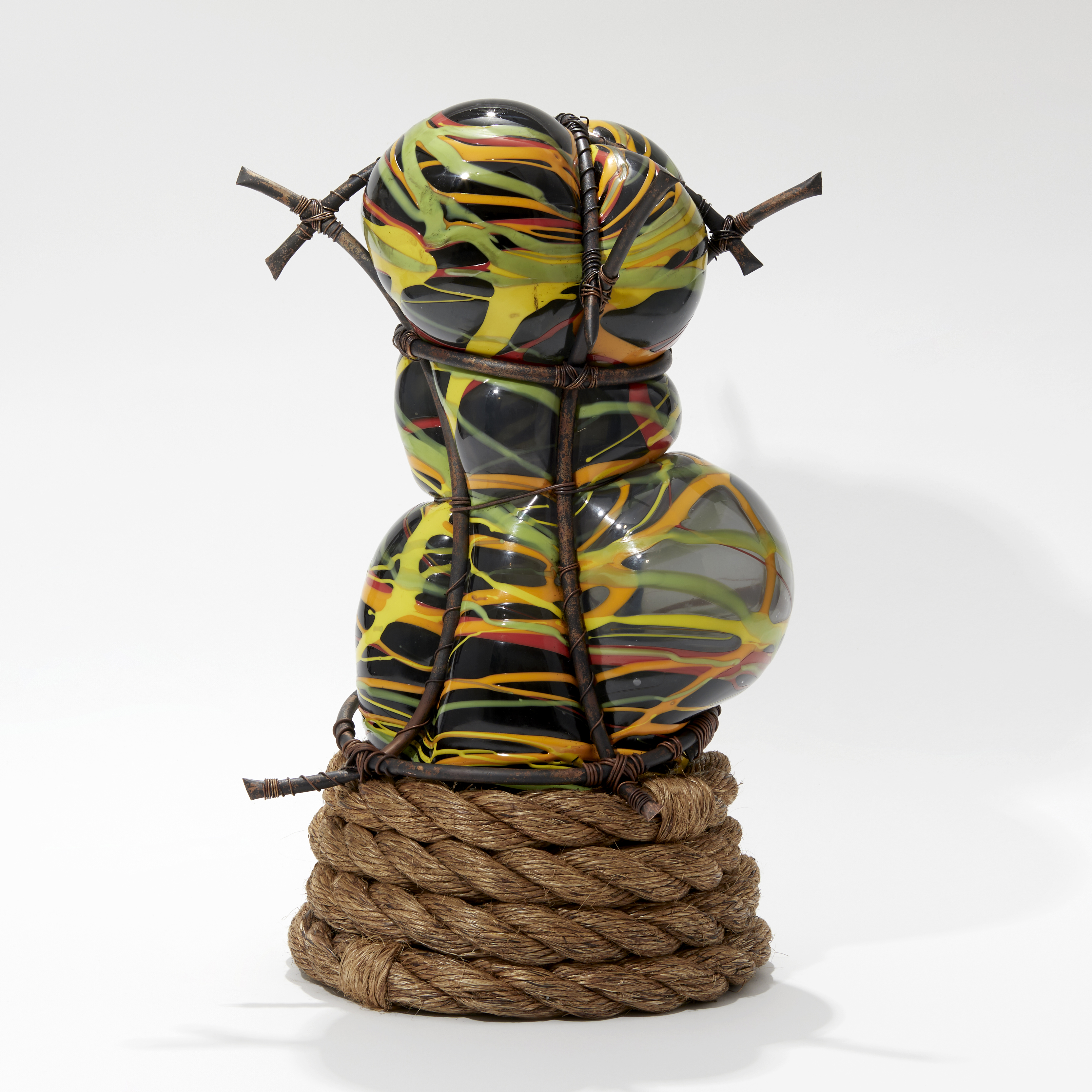 abstract figurative sculpture in grey with splashed lines in orange yellow and green set within a copper cage  with a coiled rope base