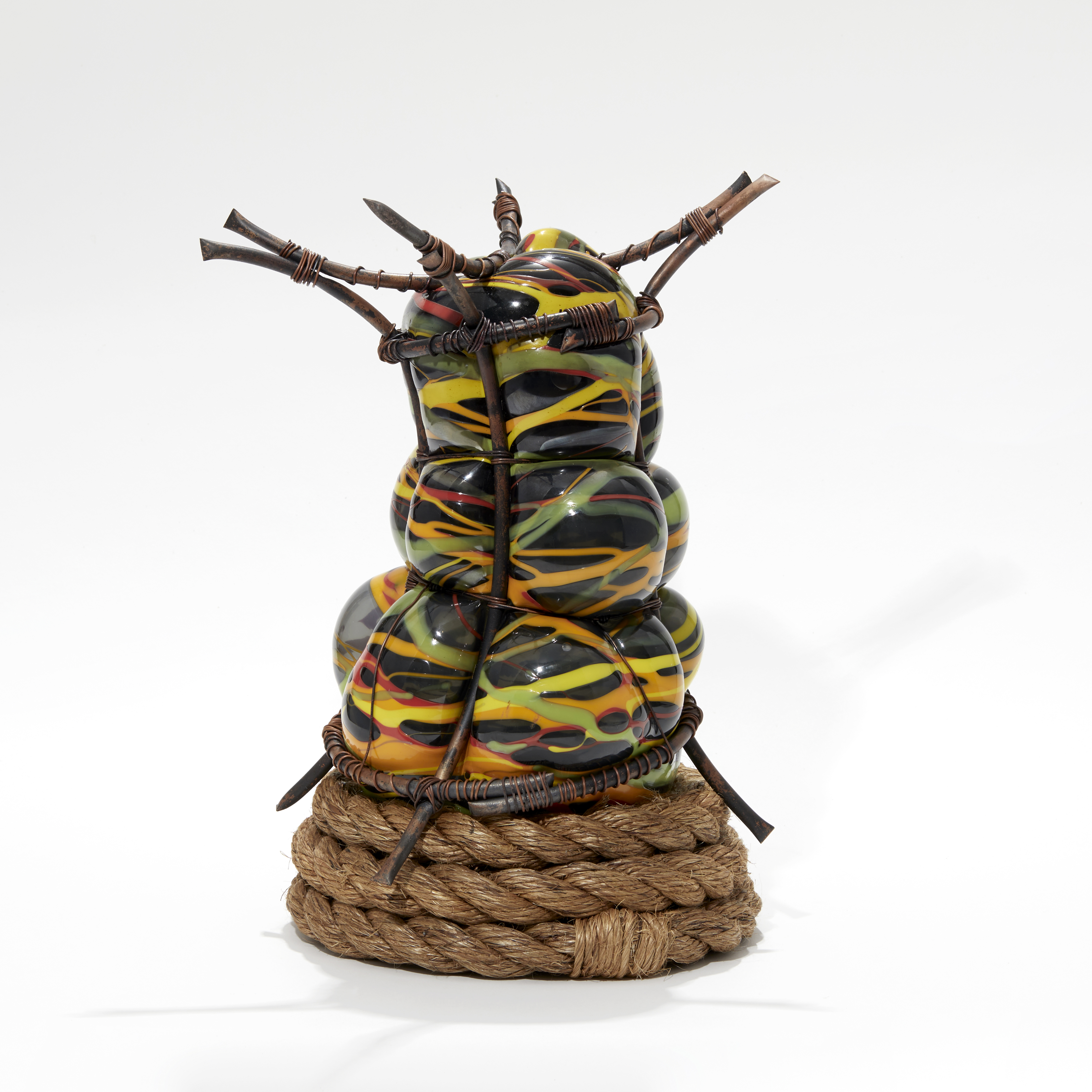 curved copper bars containing blown bulbous glass in black yellow green and orange that is bursting through the gaps with a coiled rope base