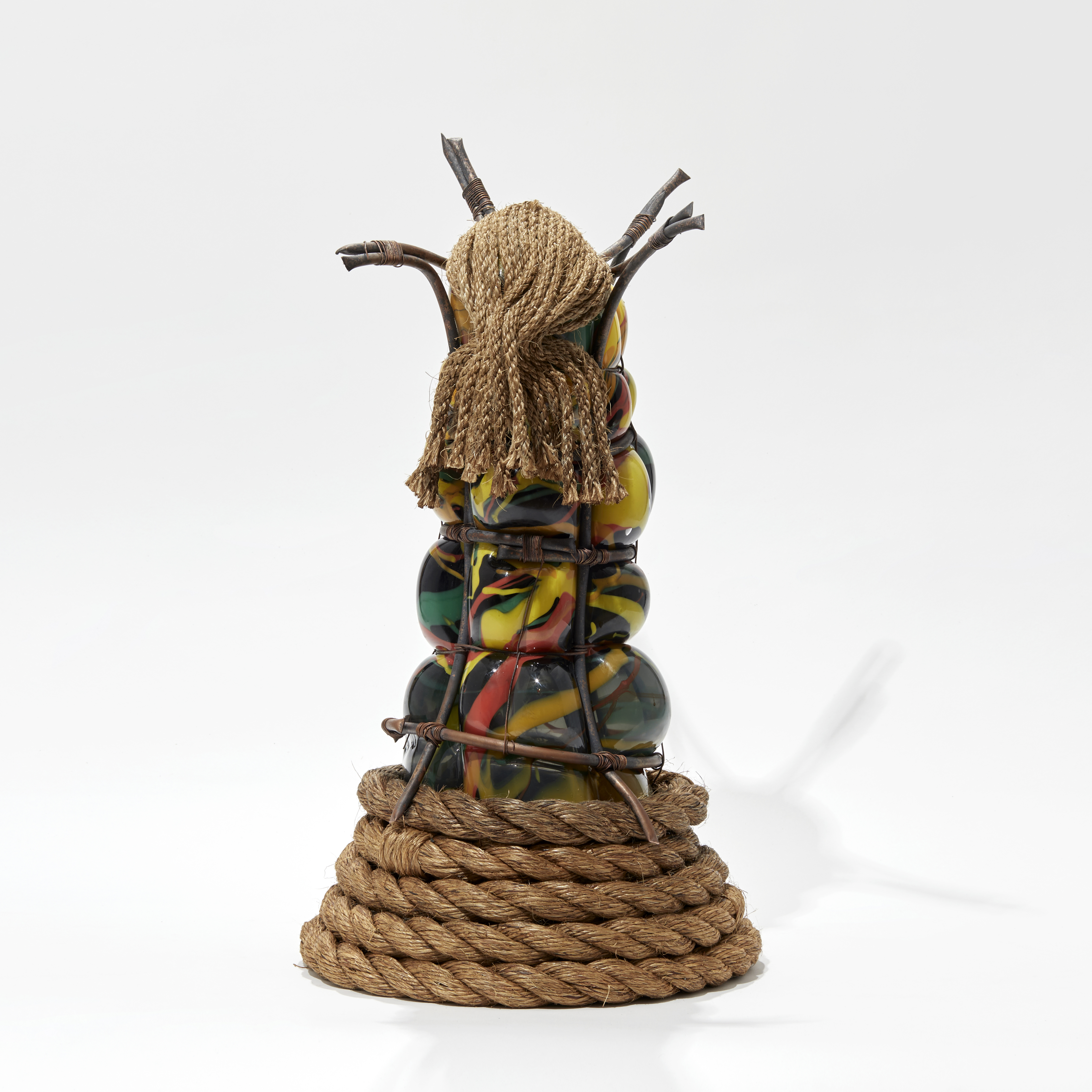 tall glass figure in black yellow orange red and green held within copper bars with rope mask and coiled rope base