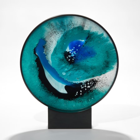 round rich aqua blue and black abstract artwork based on the evil eye amulet hand made from sheet and shattered glass framed in a black steel ring with rectangular base