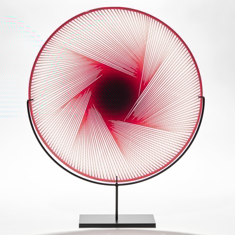 round transparent plate in clear and red glass with graphic abstract etched pattern on the top with central coloured mass with straight red lines radiating outwards hand made from glass