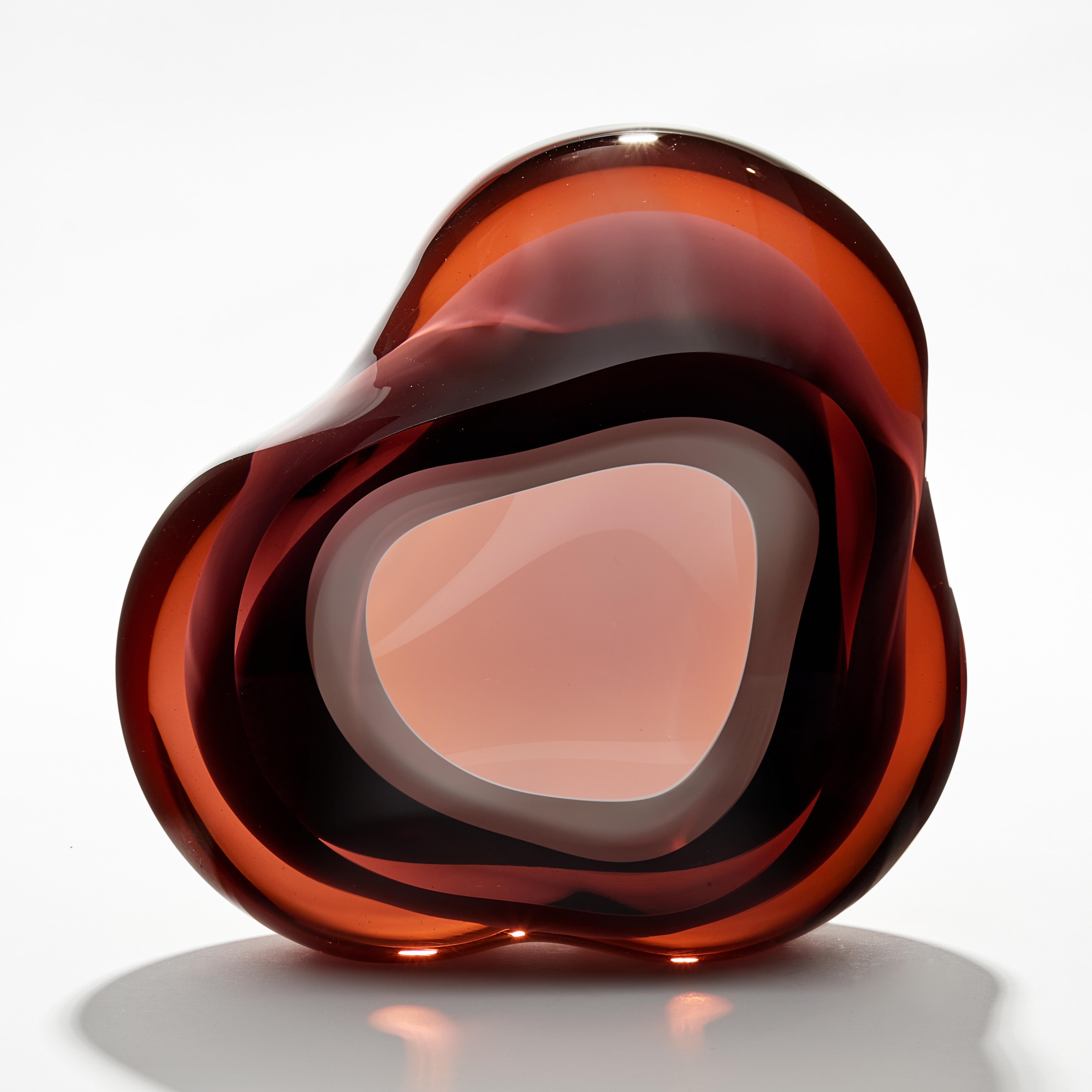 amorphous sculpture with opaque white central hole surrounded by transparent layers in dark amber peachy brown hand made from glass