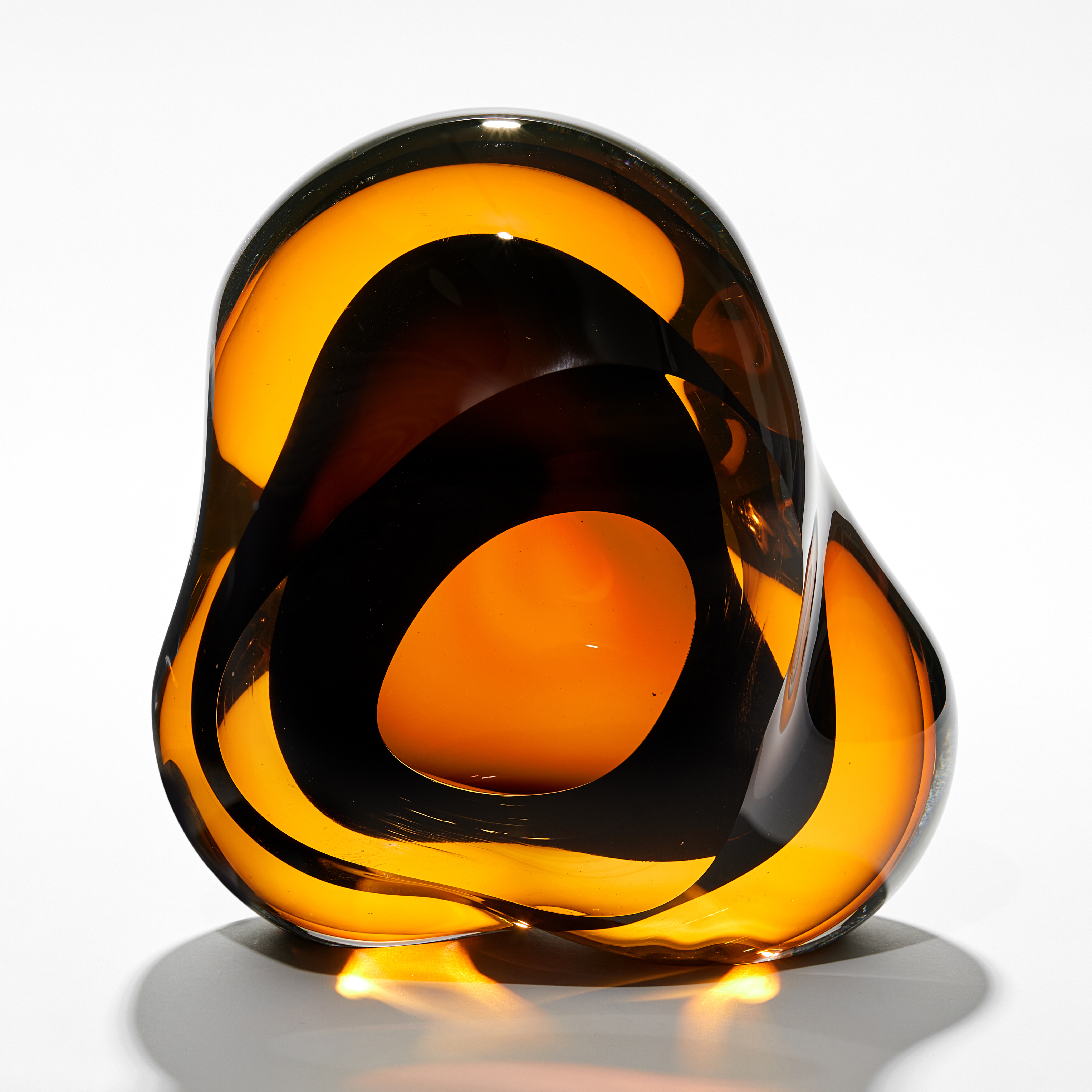 rounded amorphous sculpture created from transparent layers of bright amber and rich brown with a darker centre and organic middle hole hand made from glass