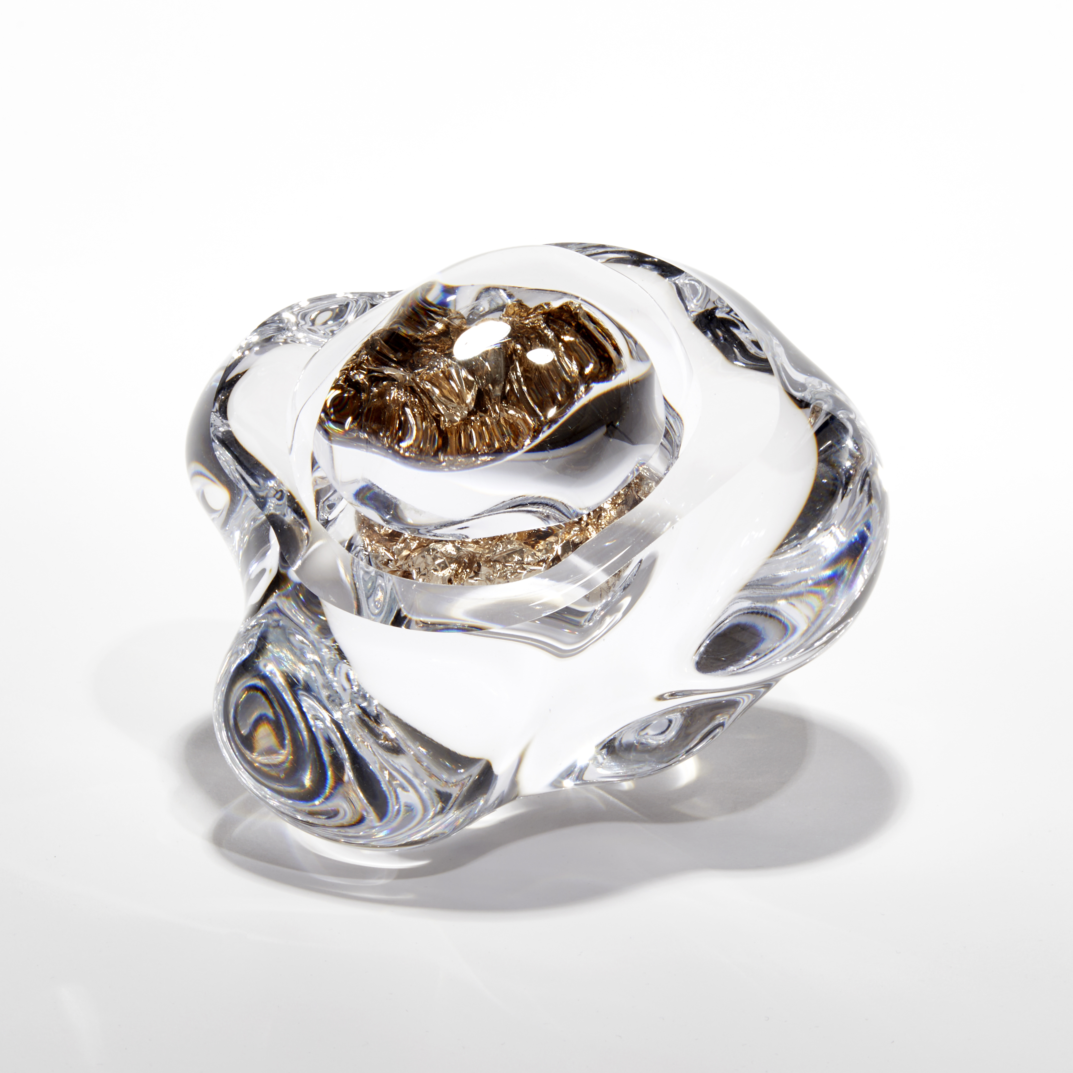 clear amorphic rock with smooth surface with densely packed champagne gold leaf trapped inside with the view warped due to the exterior mass acting as a lens hand made from glass