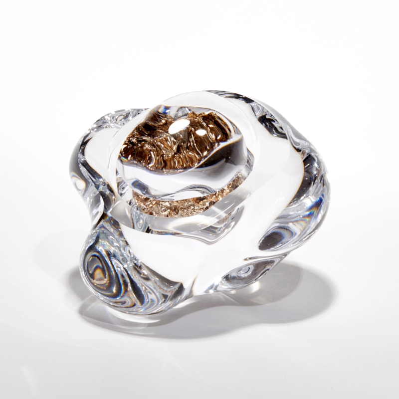 clear amorphic rock with smooth surface with densely packed champagne gold leaf trapped inside with the view warped due to the exterior mass acting as a lens hand made from glass