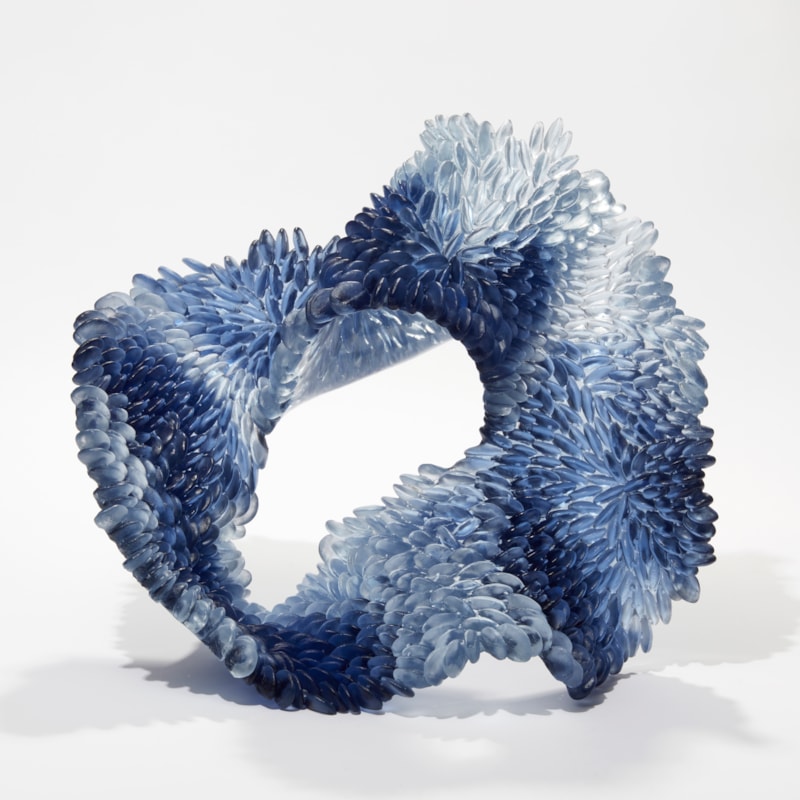 hand made standing textured looping sculpture in cast glass with scaly front surface and a polished back surface in indigo blue soft grey and clear glass
