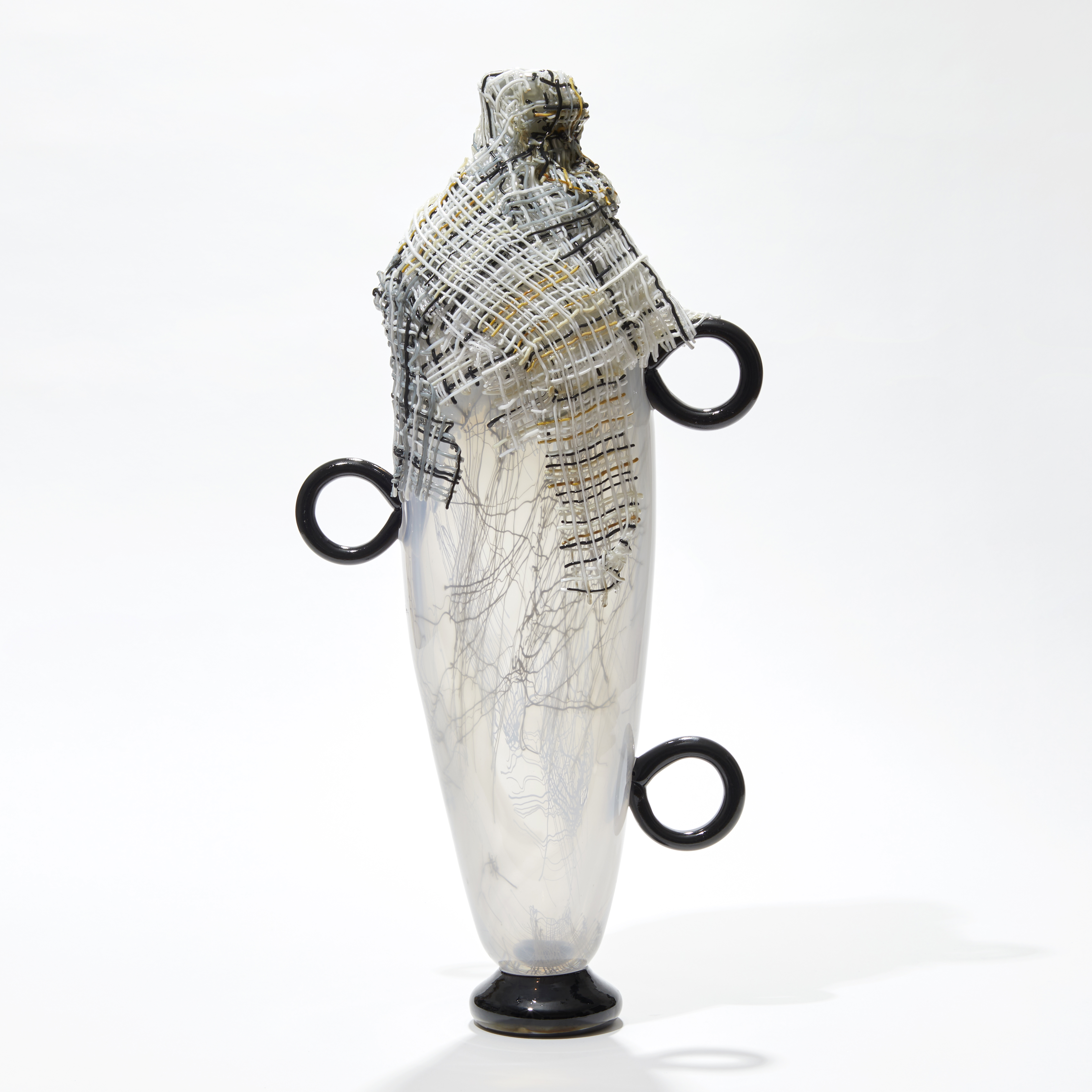 tall opaque white abstract figurative vessel with black ring handles and wrapped in multi-coloured cloth round the opening hand made from glass
