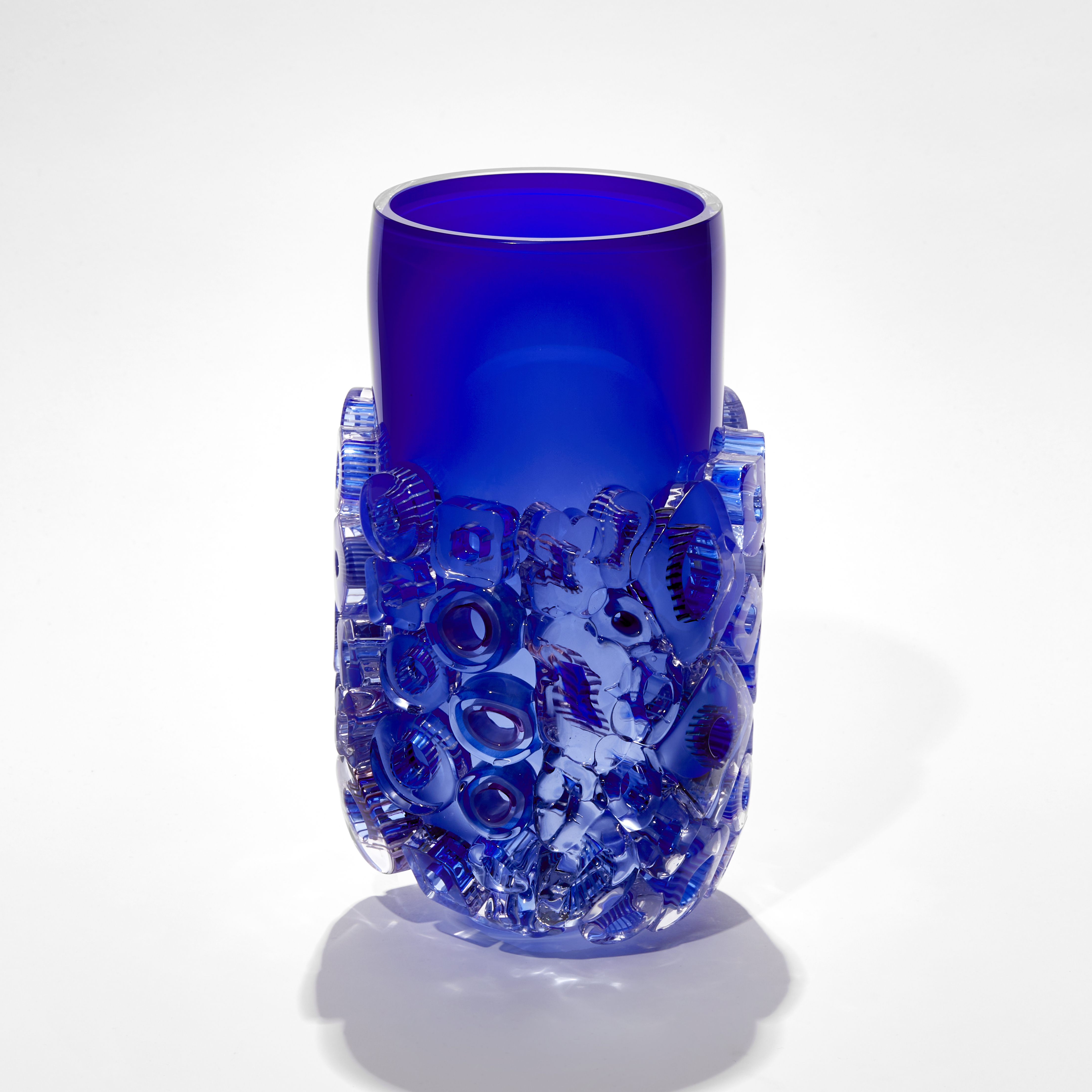 intense blue cylindrical vase with lower two thirds covered in relief decoration in circles and rings with patterns hand blown from glass