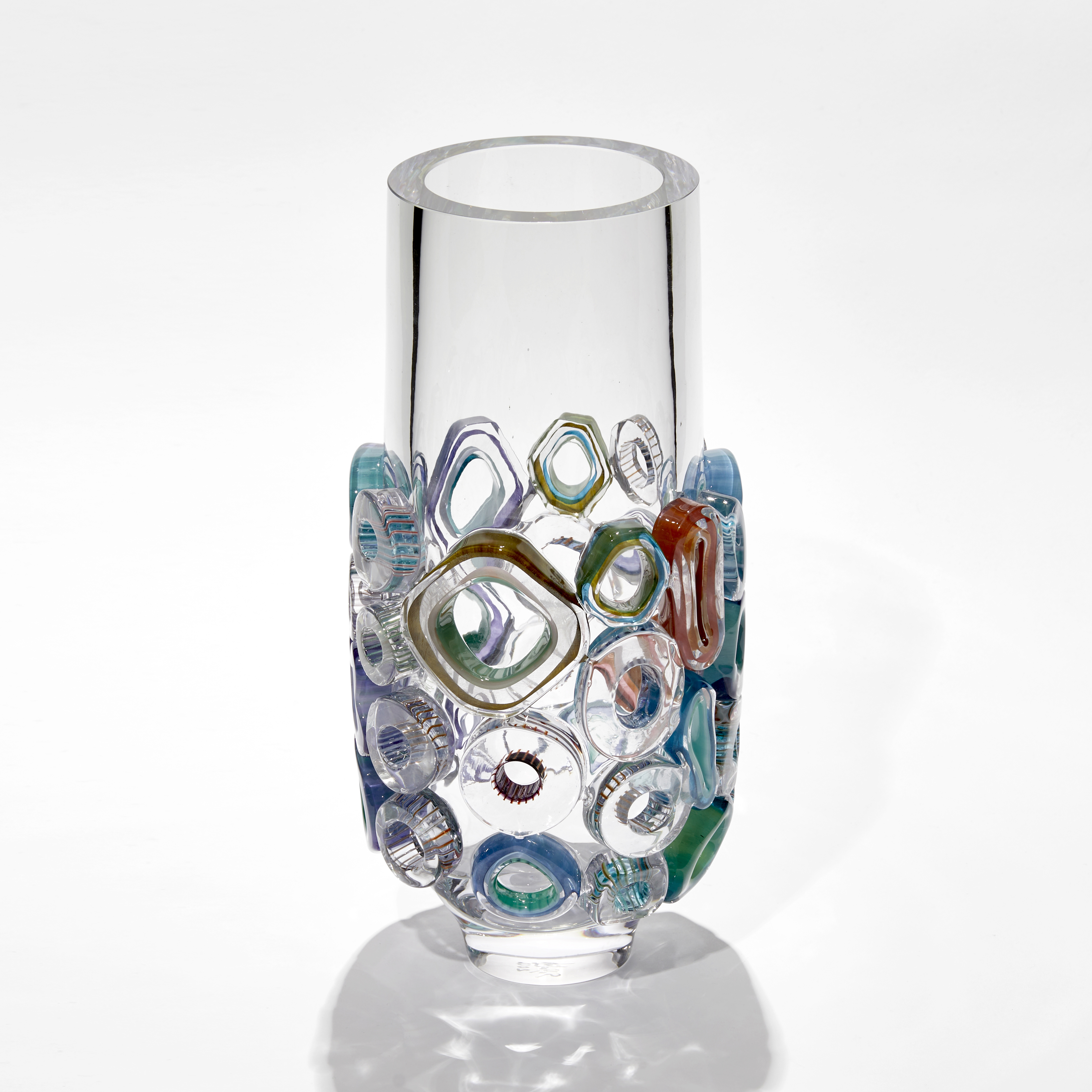 transparent tubular vase with lower half covered in raised sections in various shaped rings with different colours and patterns hand made from blown glass