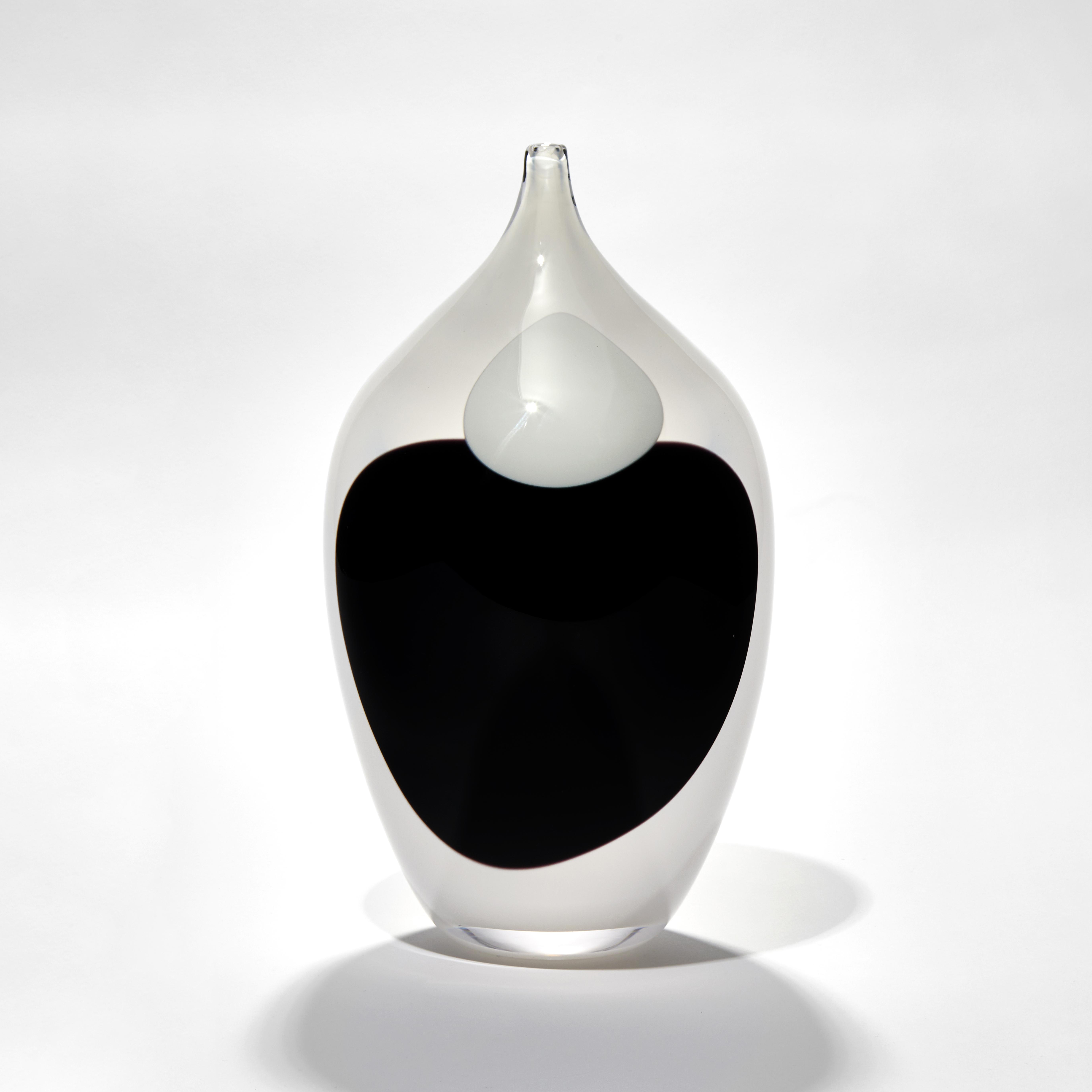 opaque white bottle with long pointed elegant neck with black and white single ink drop marks covering the front hand made from blown glass