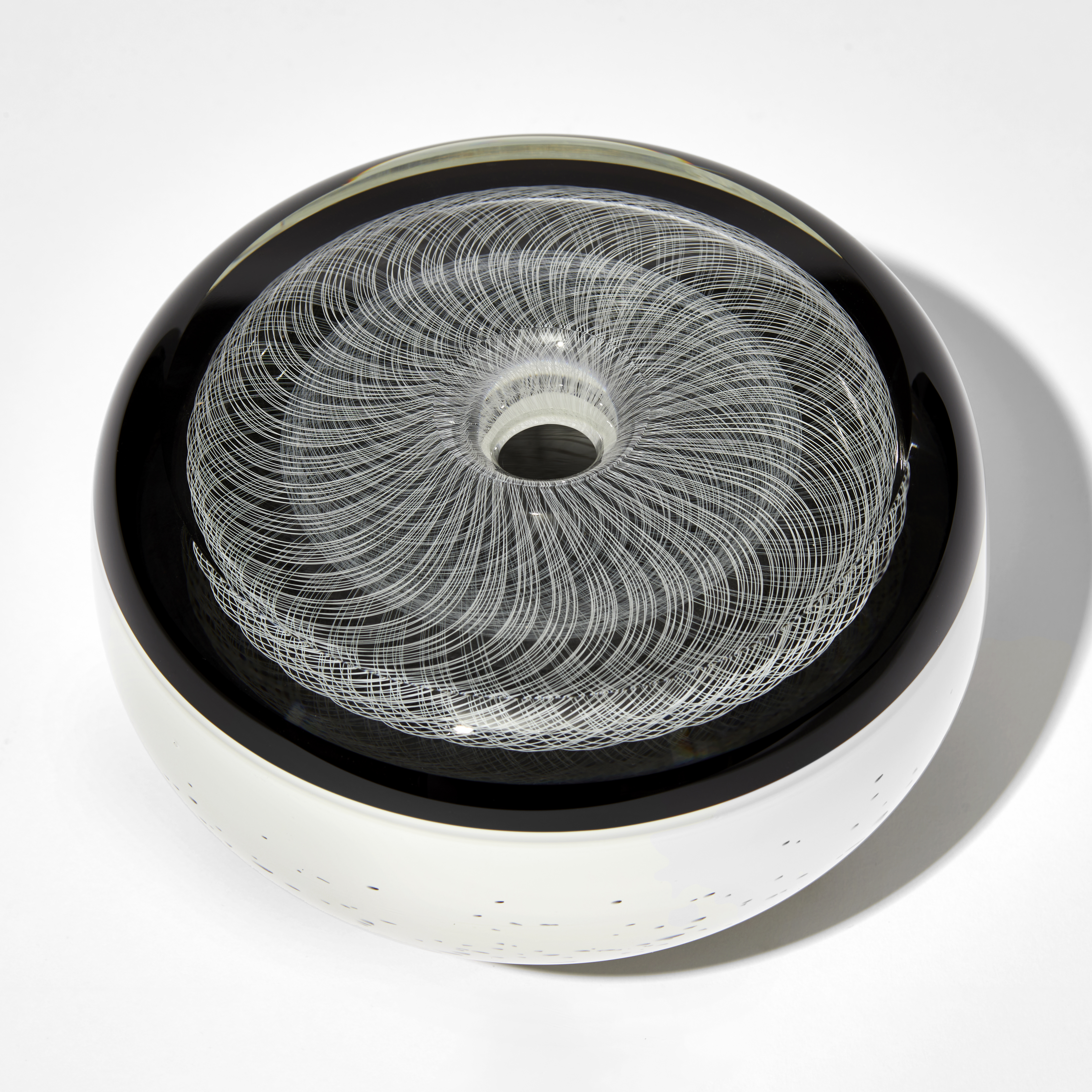 black and white vessel with flat top and rounded sides in black and white with fine filigree pattern on top and speckled base hand made from glass