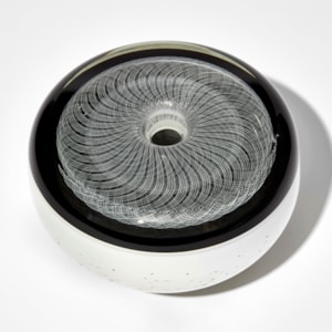 black and white vessel with flat top and rounded sides in black and white with fine filigree pattern on top and speckled base hand made from glass