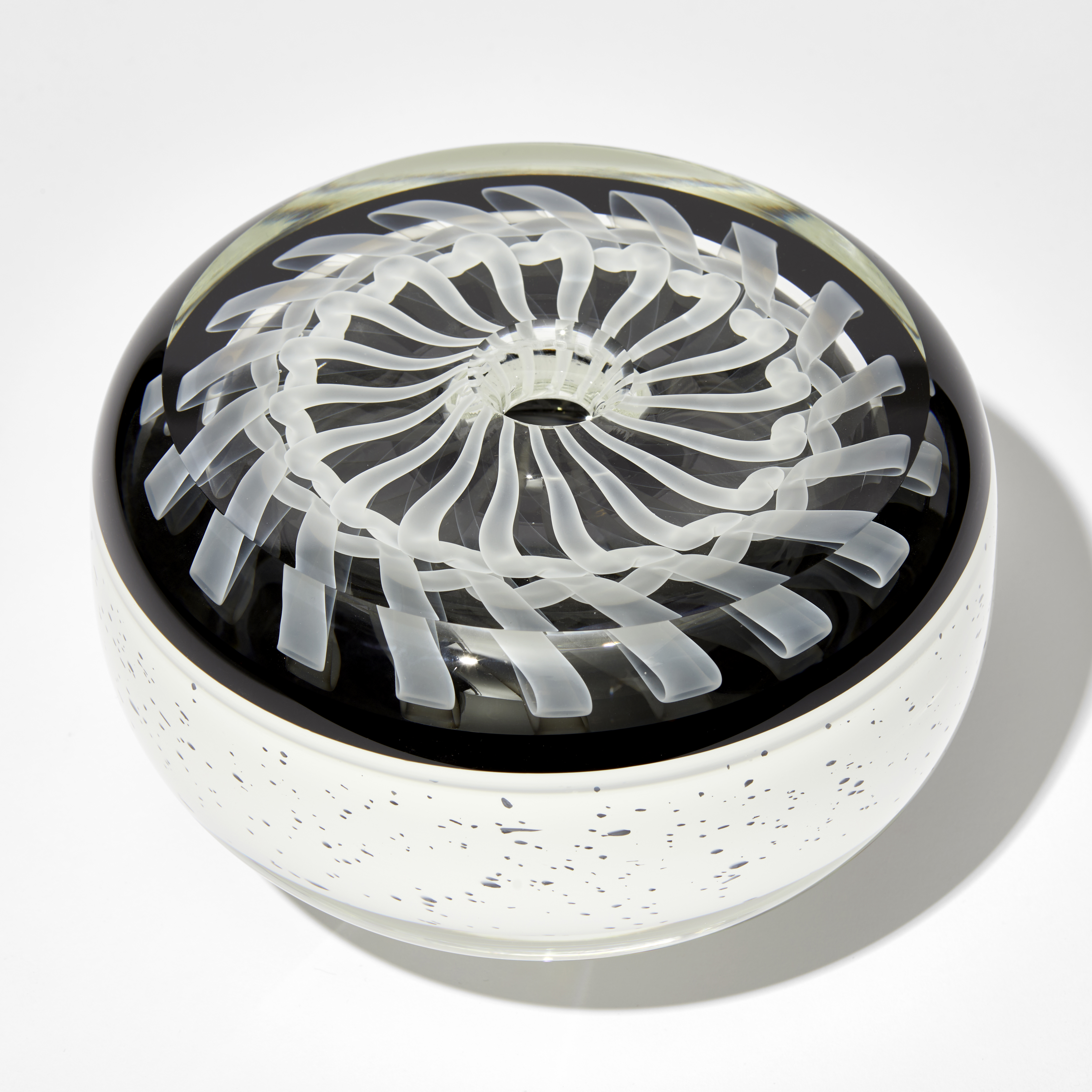 round artwork with white base speckled with black and flat top with embedded swirling ribboned white pattern on black back ground hand made from glass