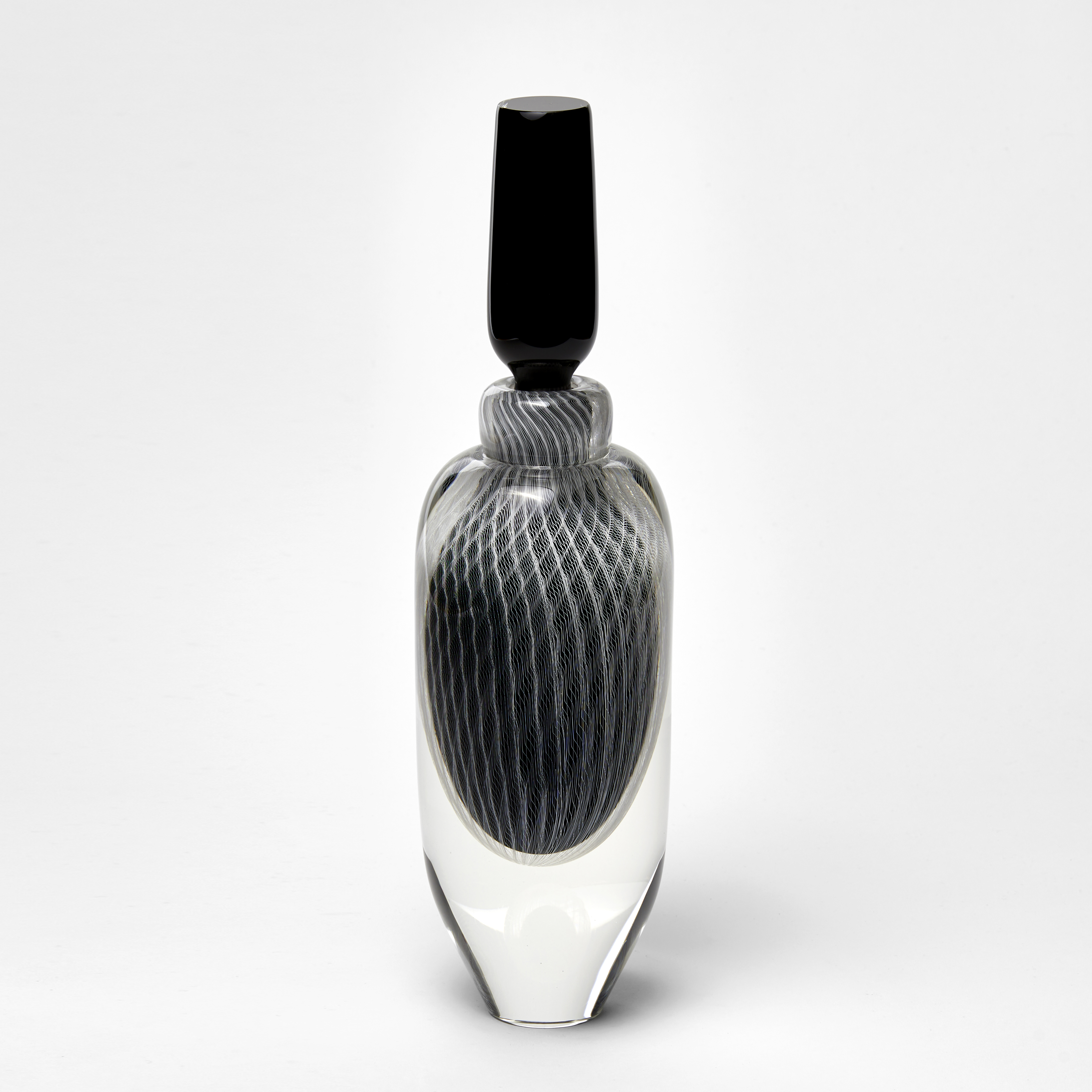 tall elegant round clear bottle with tapered base and long black stopper with fine filigree pattern trapped within hand made from glass