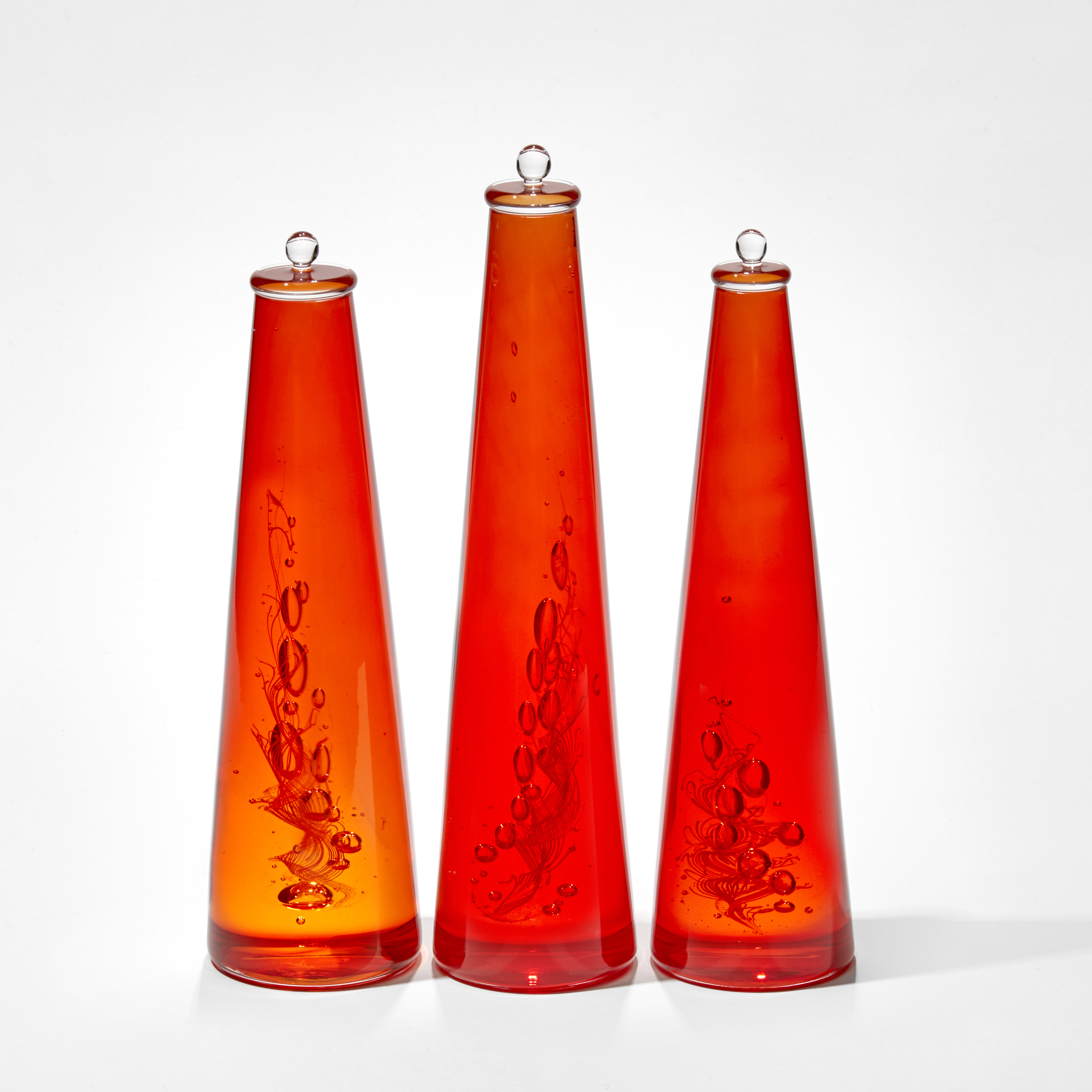 trio of bright red conical solid bottles containing trapped bubbles and a whirling helix hand made from glass