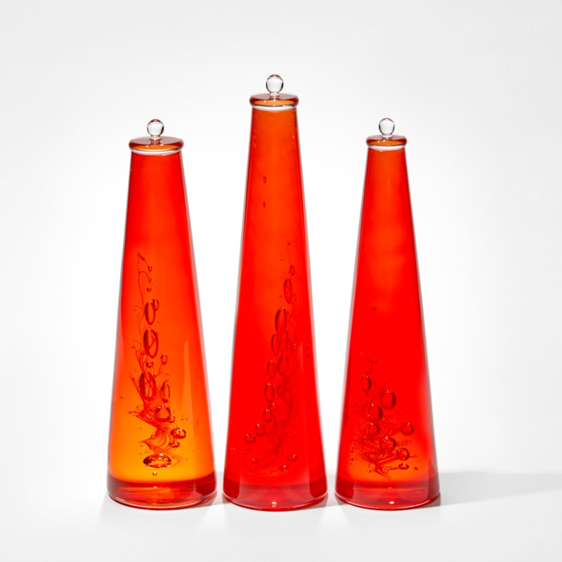 trio of bright red conical solid bottles containing trapped bubbles and a whirling helix hand made from glass