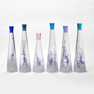 set of six conical tall bottles with fading interior from white to clear and blue lined helix detail each with a different coloured stopper hand made form glass