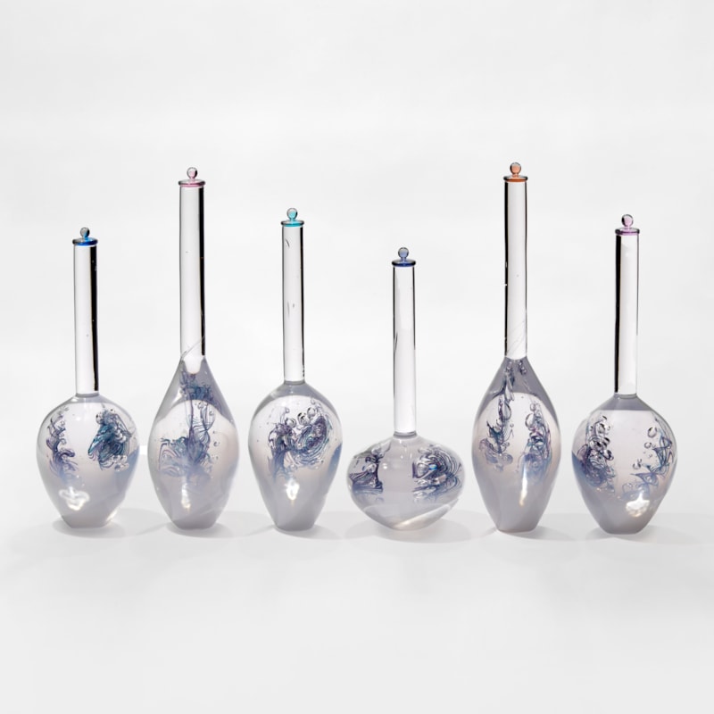 five glass bottles with bulbous white bottoms fading to clear in their long thin necks each containing a blue helix line detail and all with coloured stopper in different colours