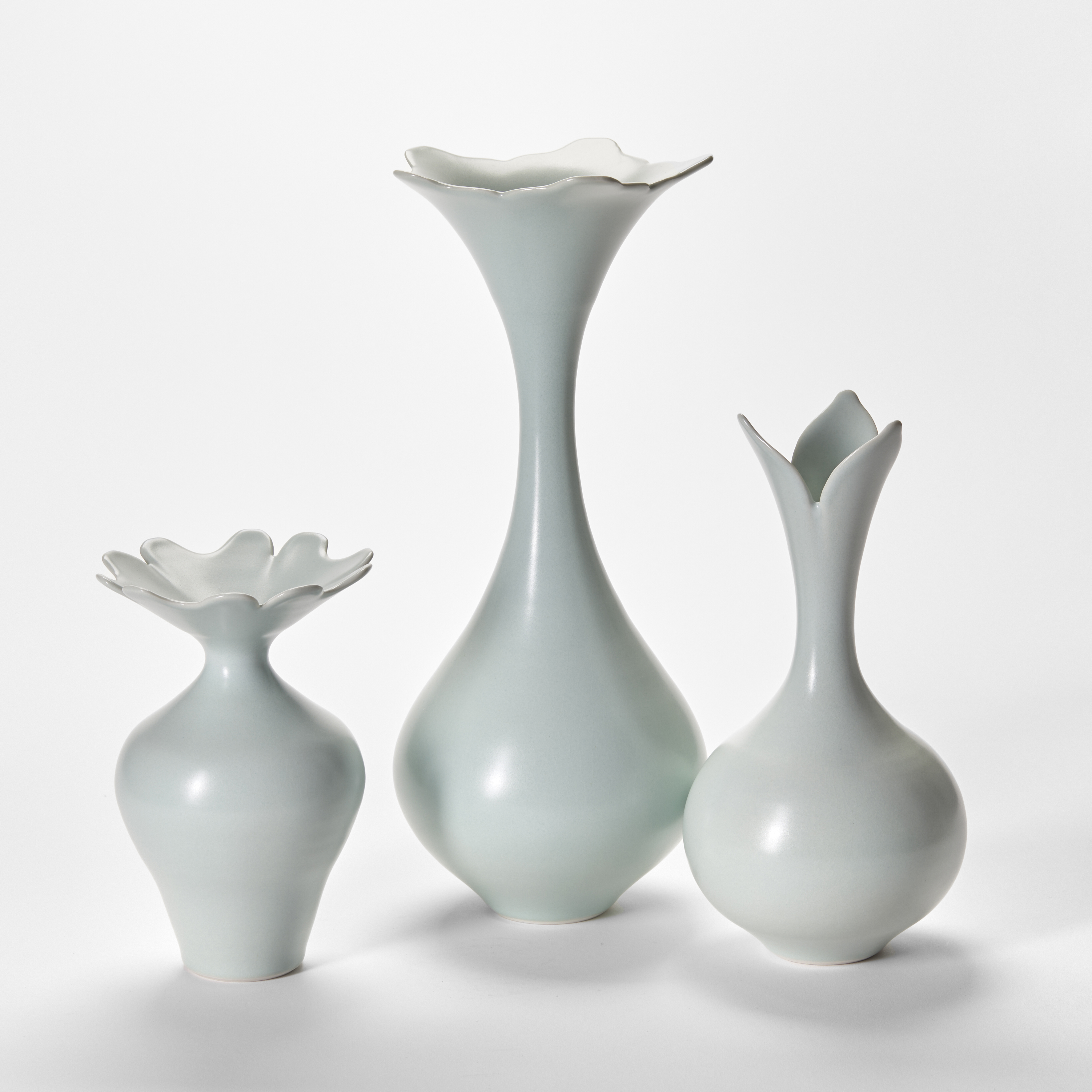 trio of celadon glazed elegant porcelain vases with round bases sweeping flaring necks and opening rims with floral cut petal details