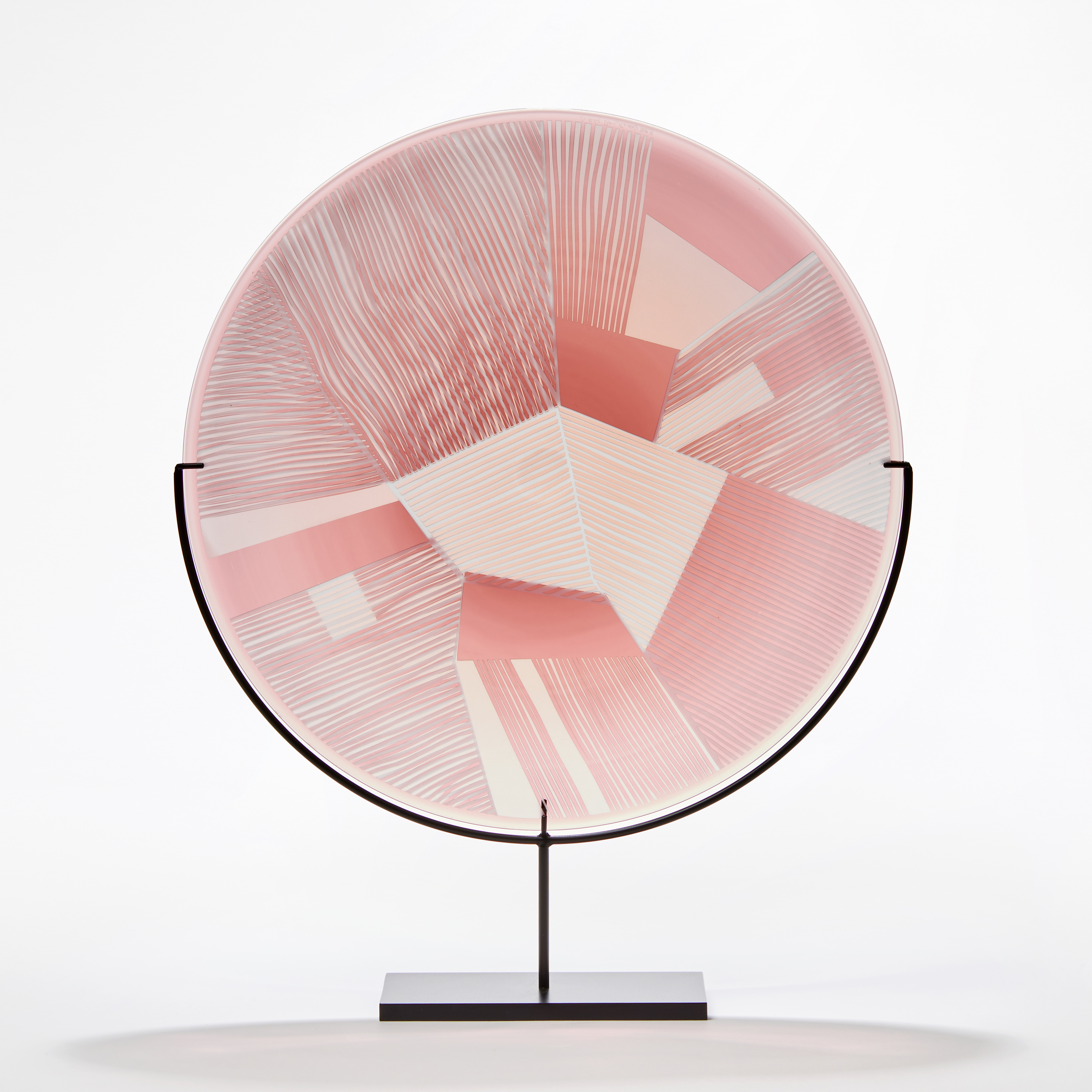 transparent grey and soft pink rondel made from blown glass with etched surface with geometric pattern presented on a black steel stand