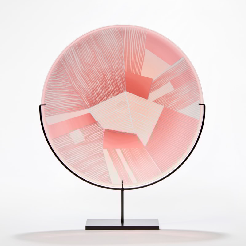 transparent grey and soft pink rondel made from blown glass with etched surface with geometric pattern presented on a black steel stand