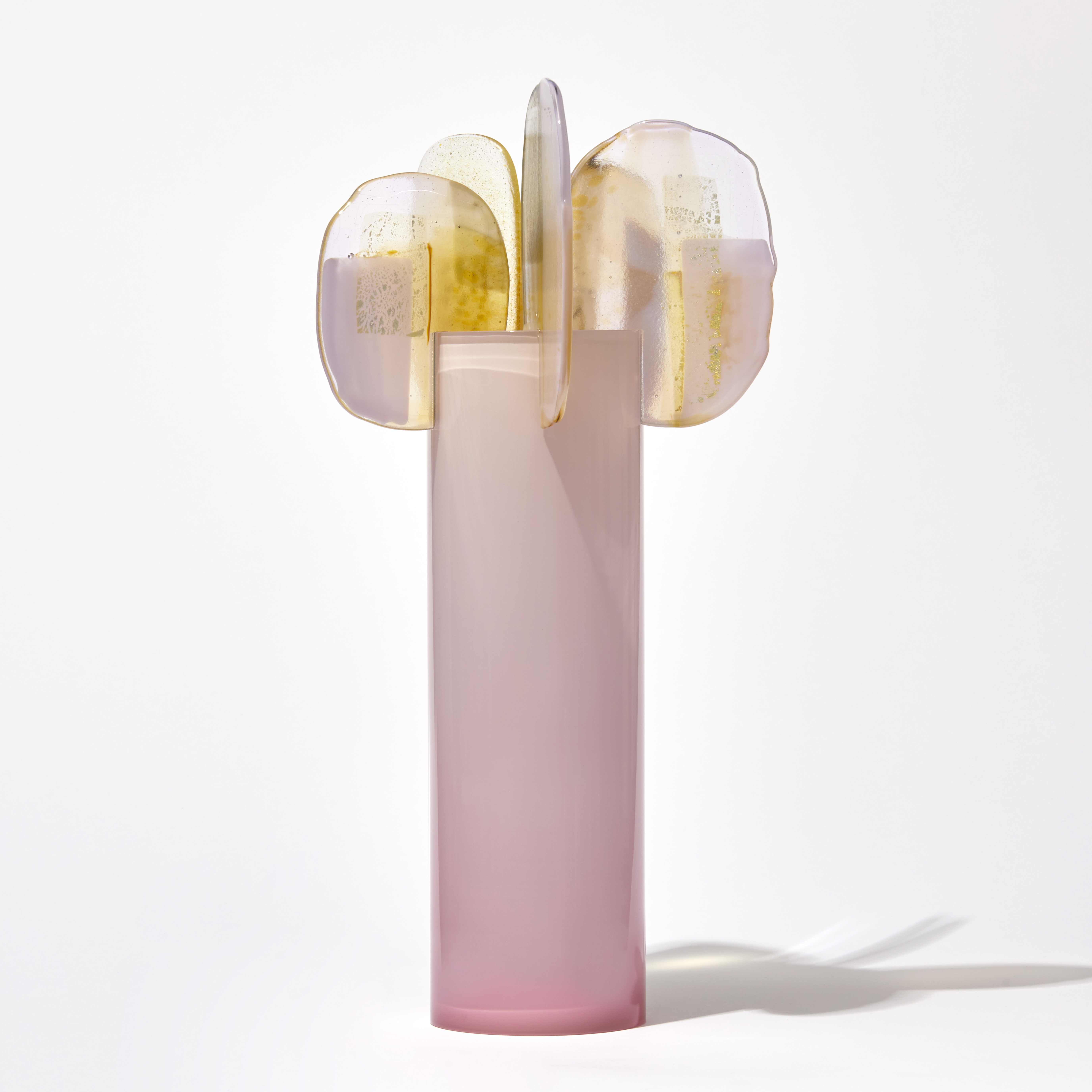 soft fading to the top opaque pink tall cylinder with five rounded finials perched on the top rim each with abstract patterns in yellow gold white and pink handmade from glass