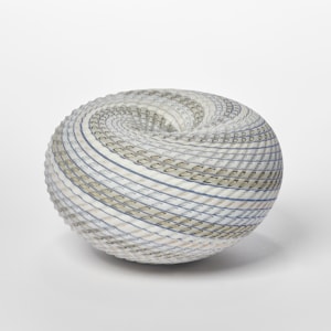 round vessel in soft blue off white blue and green with swirling lines to the dipped vortex centre with lines both coloured and cut within the surface handmade from glass