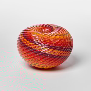 round textured orange yellow and aubergine purple striped vessel with central dipped opening with straight cut recessed lines swirling around the piece hand made from glass