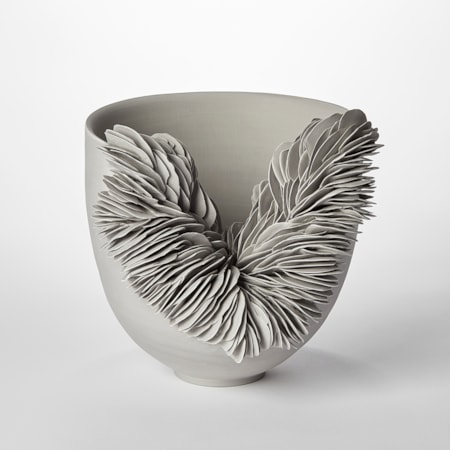 tall sided light grey round bowl with front third cut away with the gap filled with stacked shards with a scale like appearance hand made from coloured porcelain
