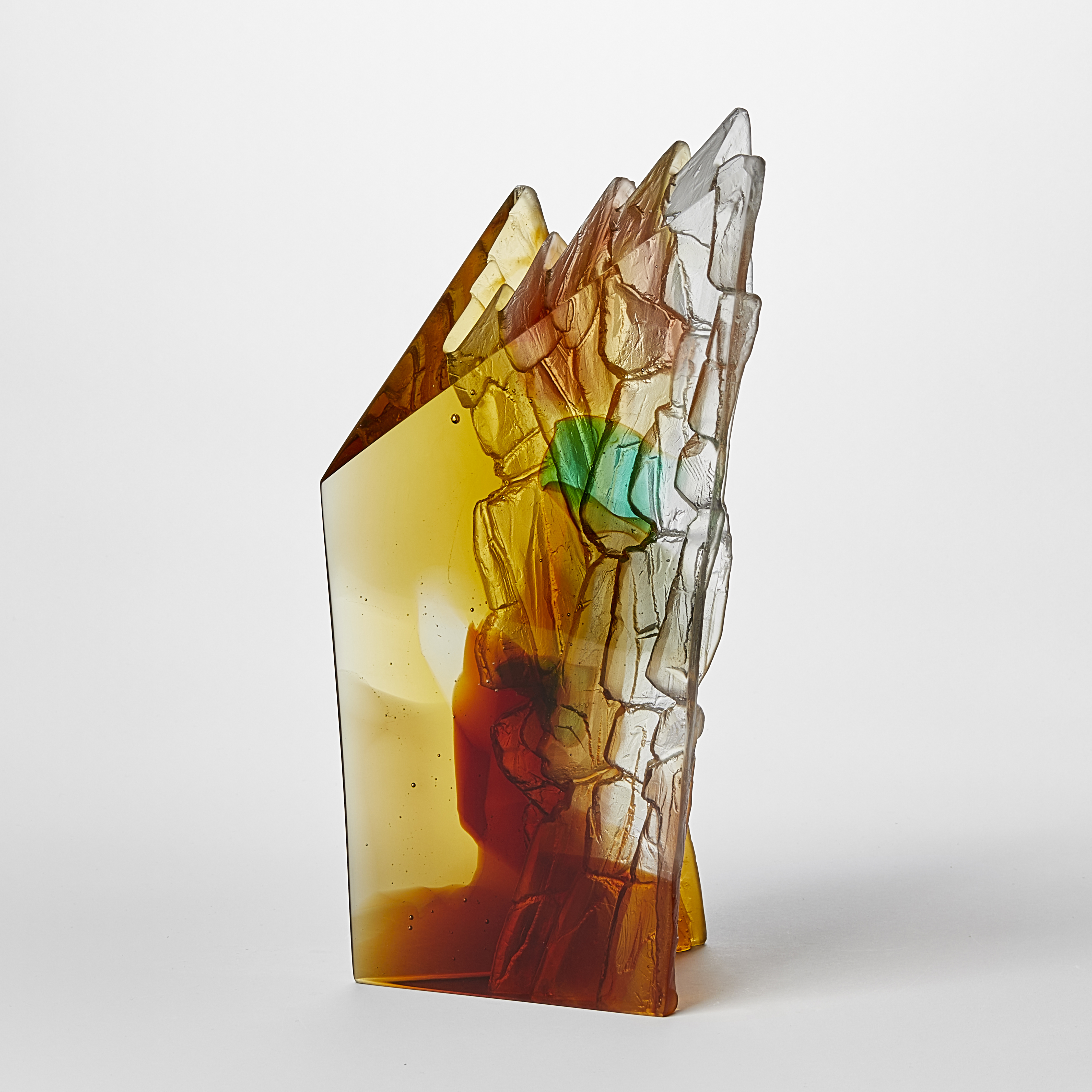 angular free standing amber rust green and yellow transparent sculpture with two flat polished surfaces and two inner ones with rugged and textured detail hand made from cast glass 