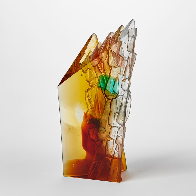 angular free standing amber rust green and yellow transparent sculpture with two flat polished surfaces and two inner ones with rugged and textured detail hand made from cast glass