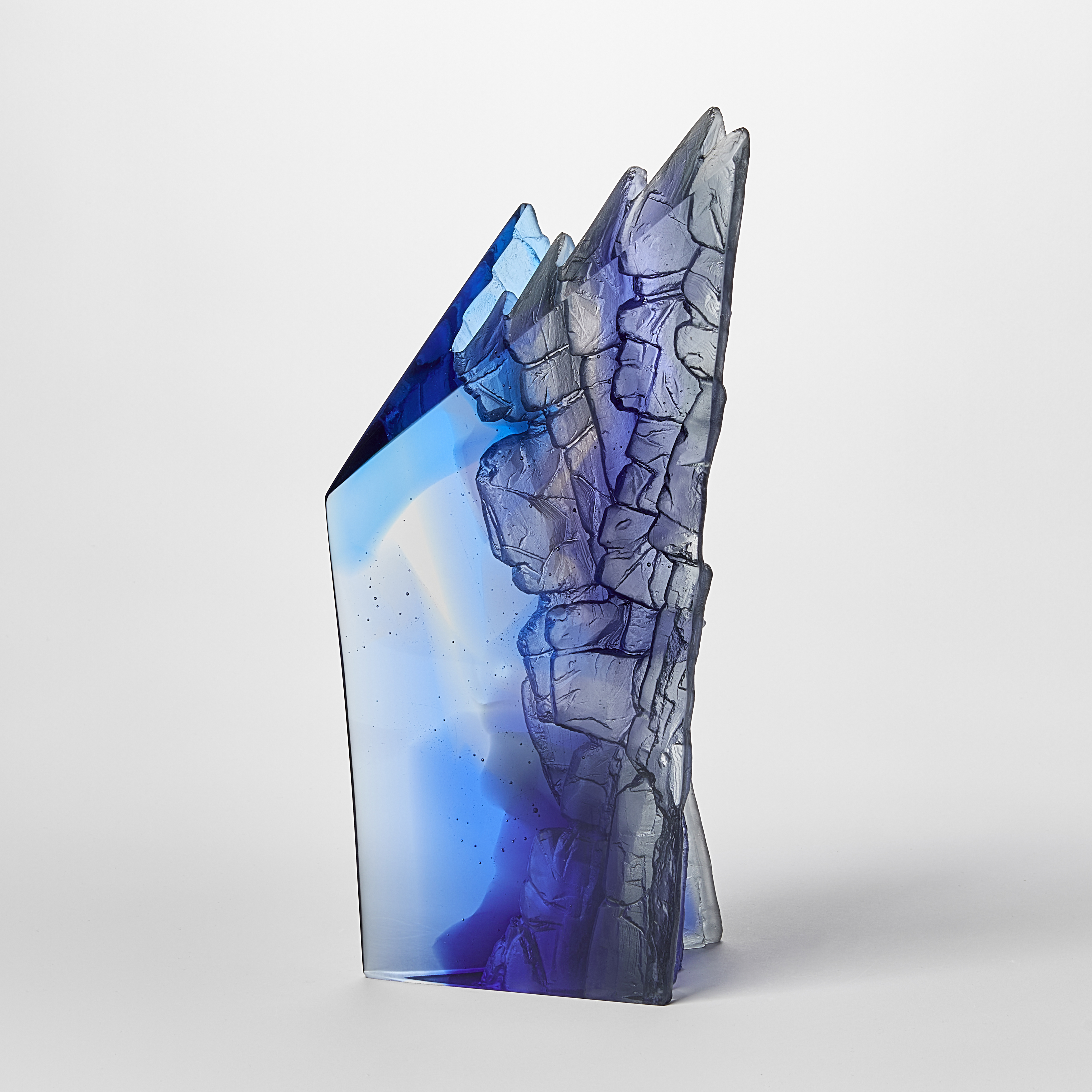 mixed blues cast glass sculpture inspired by rocky cliff edges with angular form and two polished sides with two additional sides covered with intense rough detail
