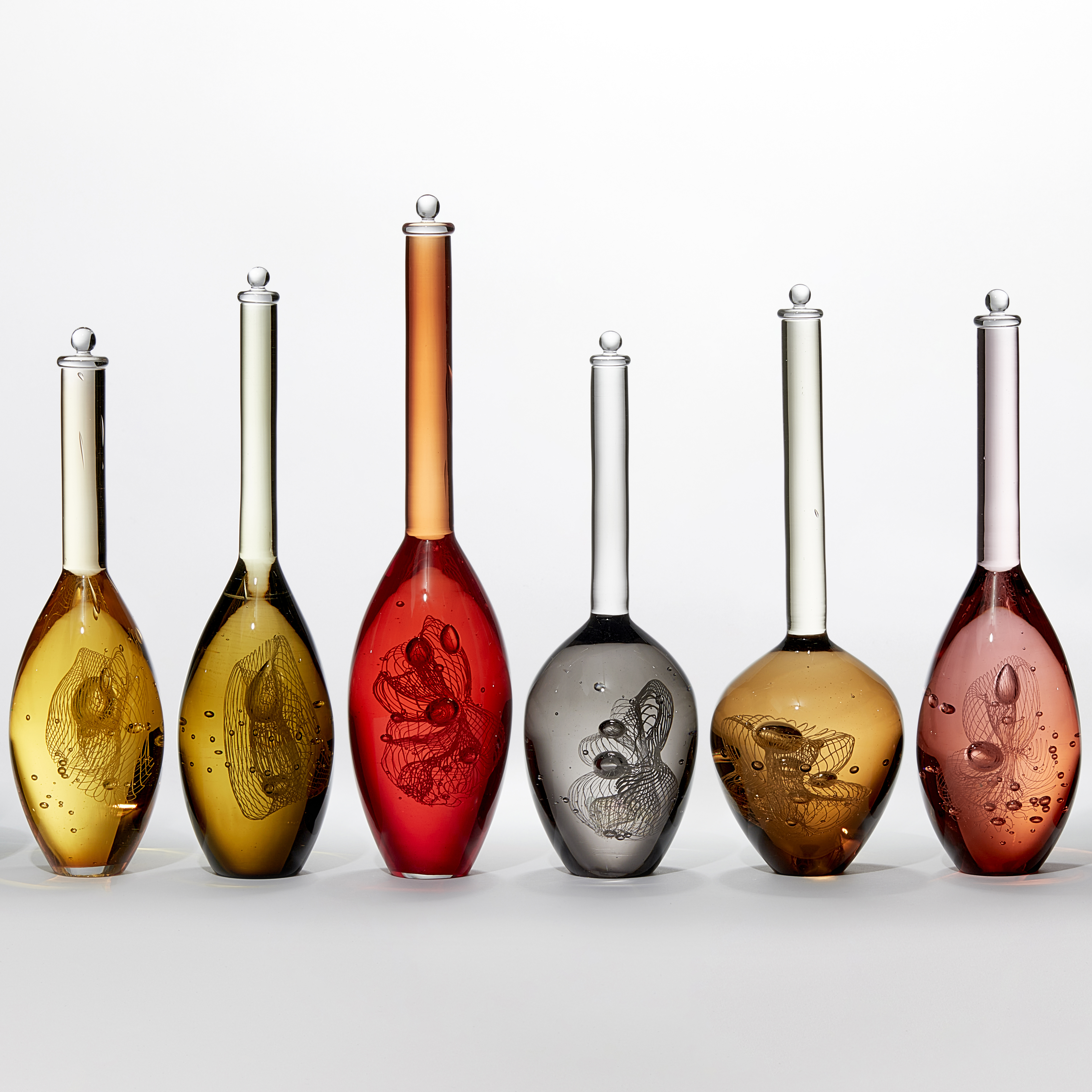 series of nine solid scientific looking bottle forms in various transparent warm colours sea green amber orange red bronze gold peach and grey each with a spiralling helix detail inside hand made from glass