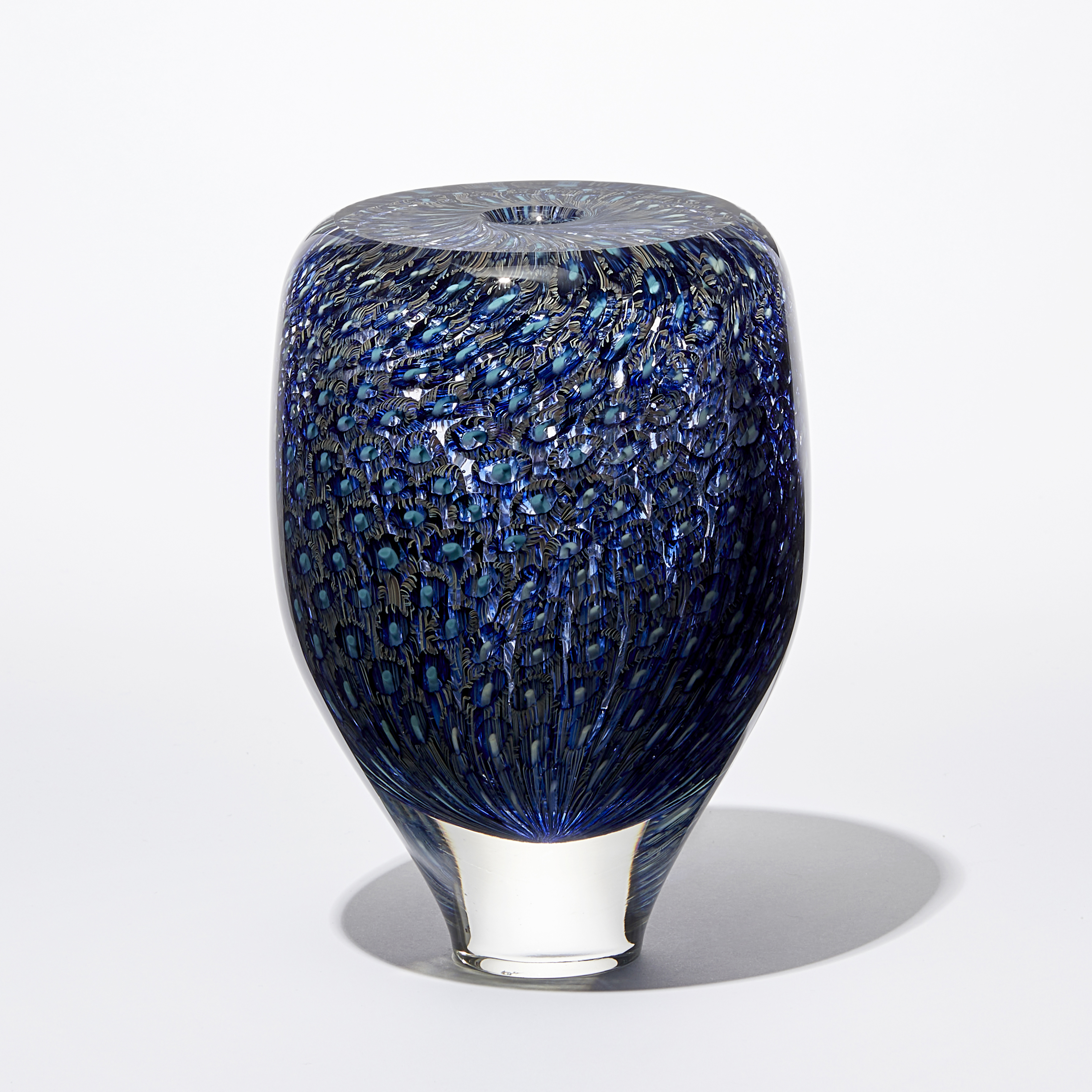transparent rounded vessel with tapered base with flat top and central opening covered in an intense detailed pattern in rich blue turquoise and aquamarine hand made from glass