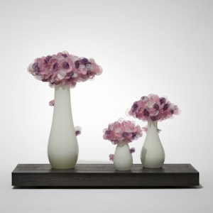 a trio of abstract trees each with an sleek alabaster coloured trunk topped with a multitude of sugary candy cane pink coloured lolliop leaves hand made from glass and presented on a rectangular wooden base
