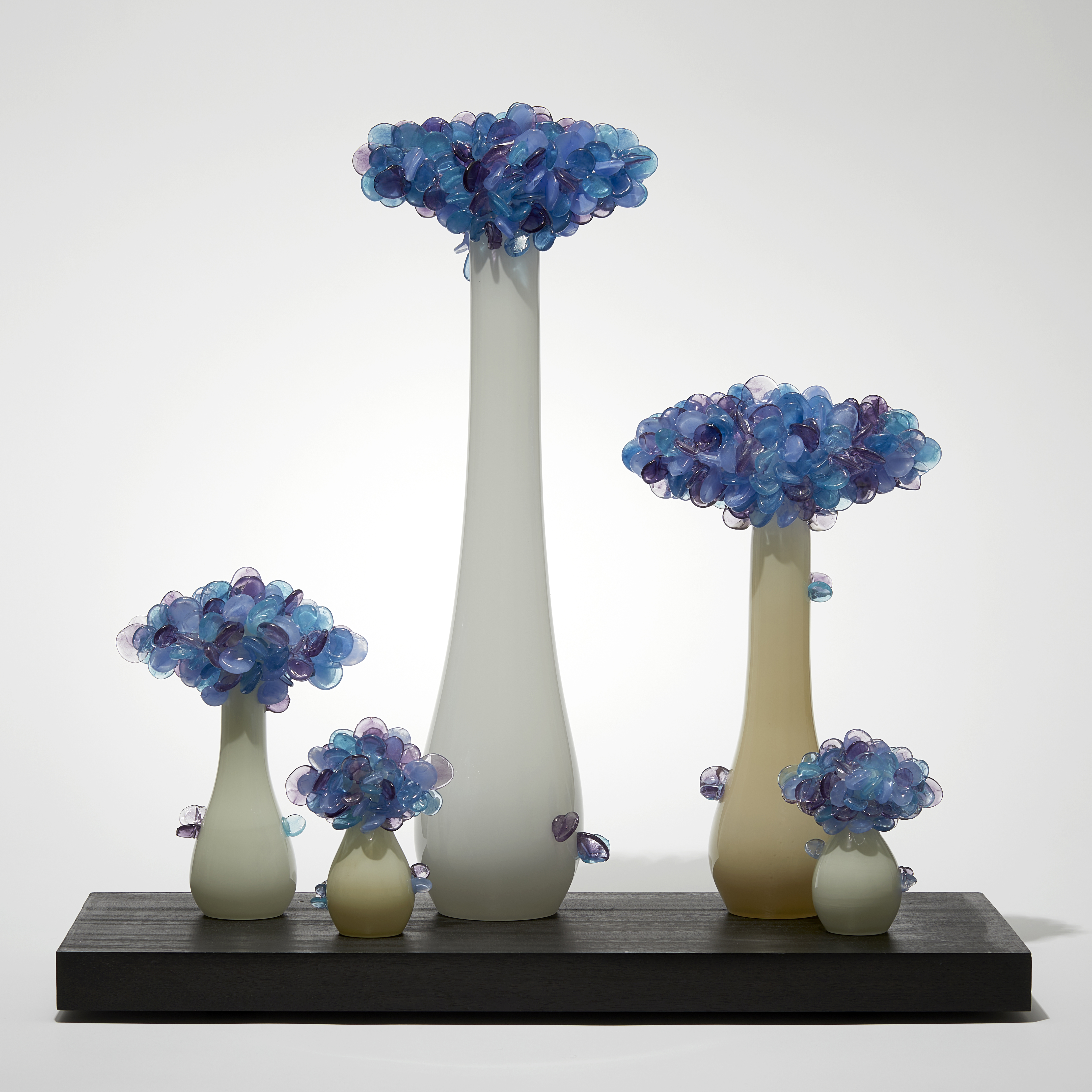 rectangular black wooden base with bonsai inspired trees set on its top each with bulbous rounded bases and clusters of lollipop shaped various blue and purple leaves hand made from glass