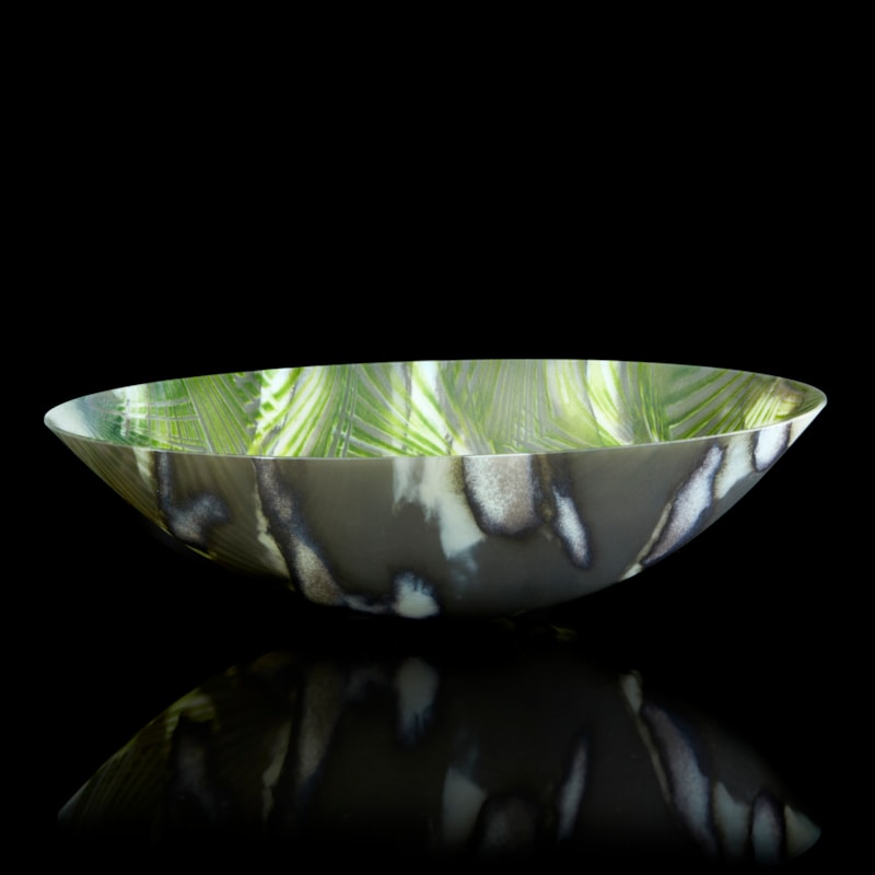 oval bowl with sweeping sides and rounded base with palm tree interior repeat pattern and exterior camouflage pattern in a myriad of greens hand made from glass
