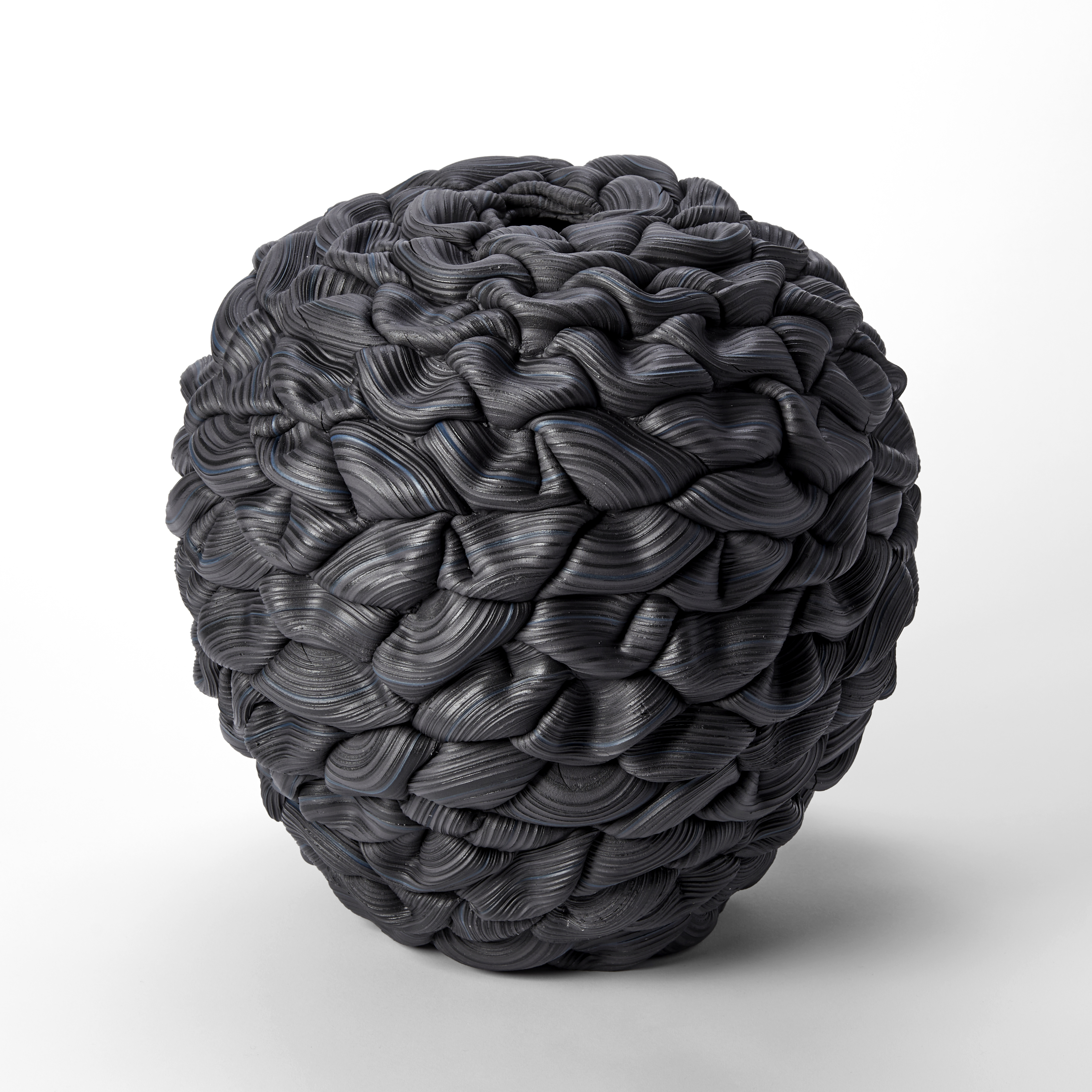 black and blue round vessel with the appearance as if made from interwoven and stacked ridged thick black rubber bands each creating soft folds and layers hand made from porcelain and parian 