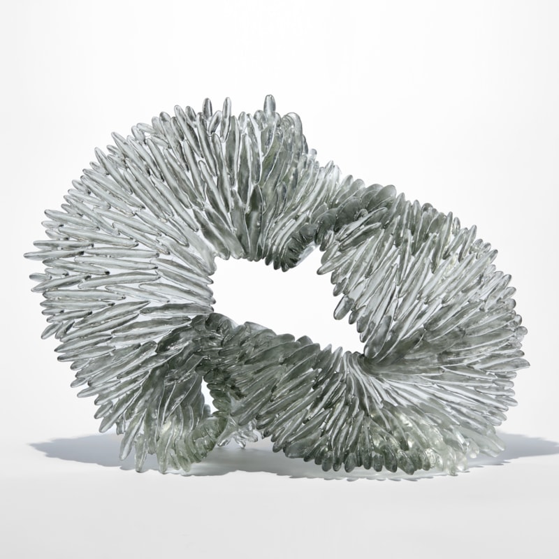 clear and grey stood organic looped drooping form with one side flat and shiny the other covered in raised fins like the gills of a mushroom hand made from cast glass