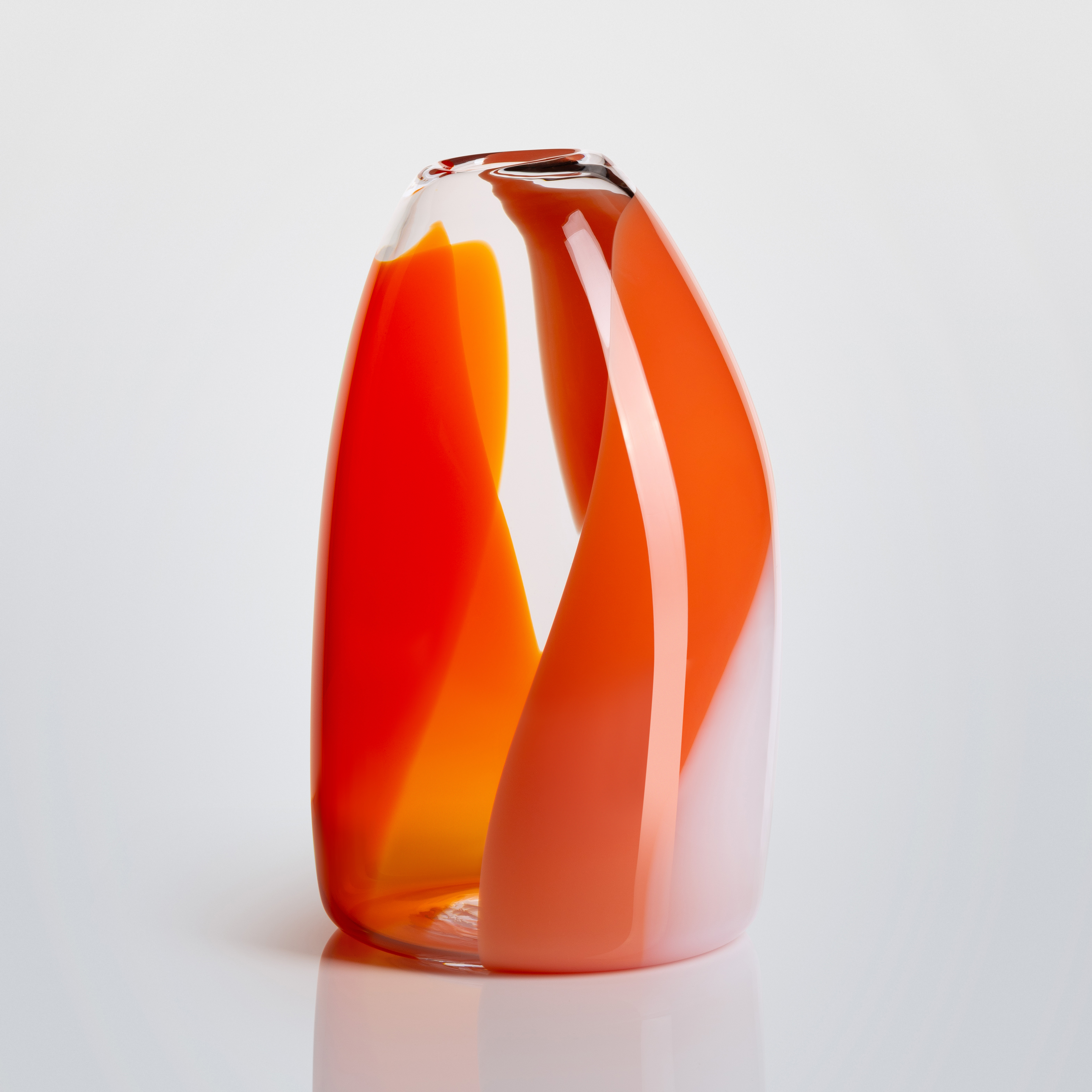 curved narrowing at the top tall transparent glass vase with soft hazy bands of colour in orange red coral and pink curling round the form hand made and blown from glass 