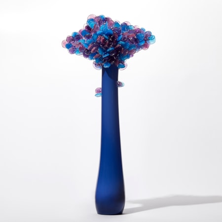 tall tree sculpture with long elegant thin trunk in opaque royal blue with diamond shaped canopy covered in lollipop shaped leaves in blue purple and lilac hand made from glass