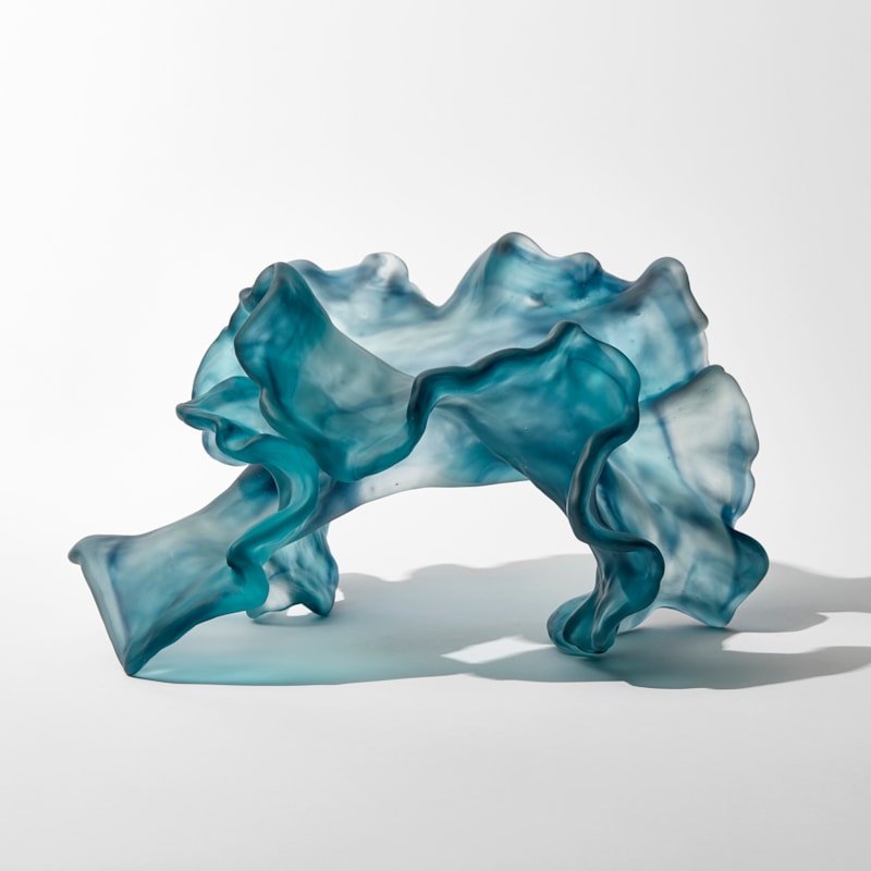 abstract swirling clear and jade blue sculpture with the appearance of a piece seaweed floating under water with frilled edges hand made from cast glass