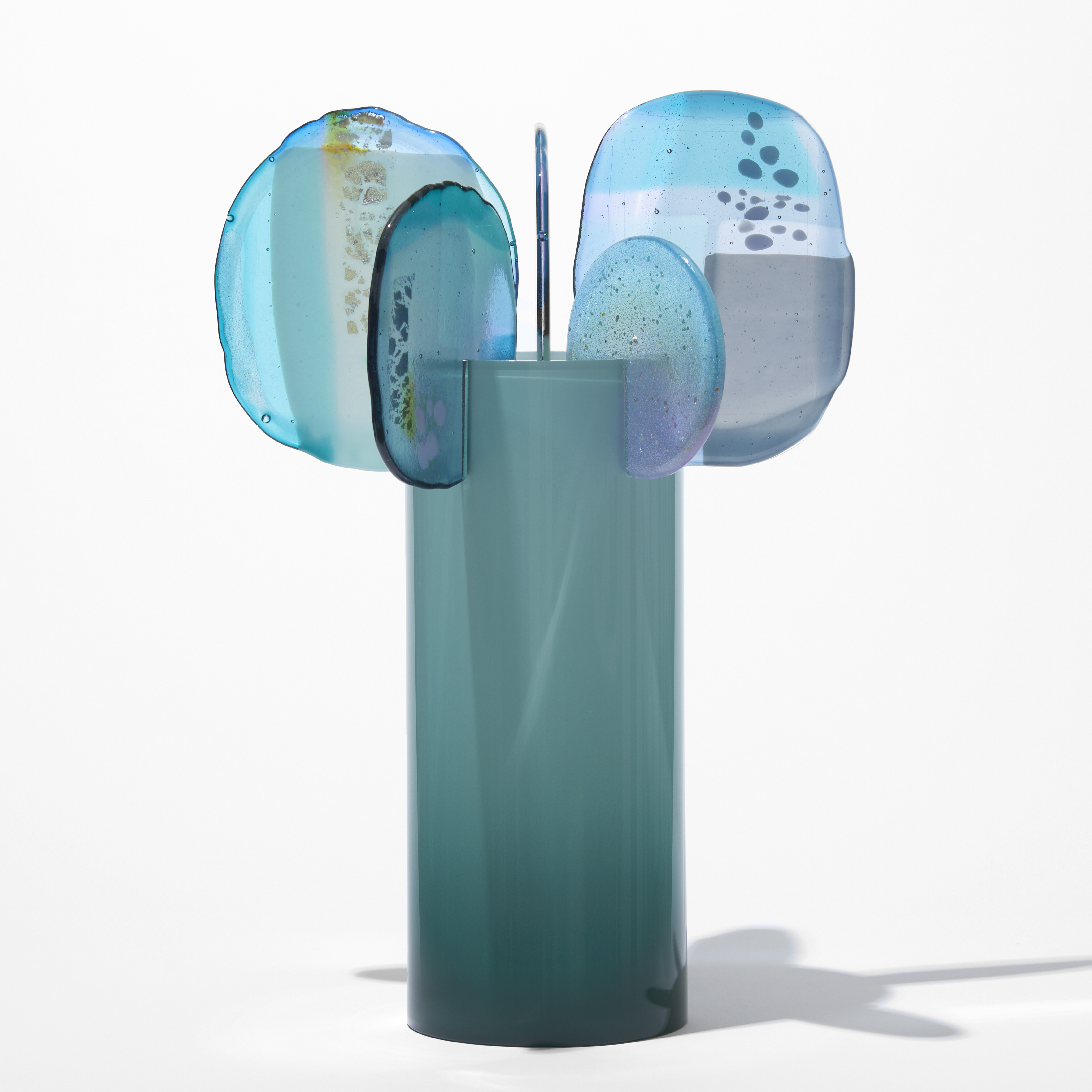 opaque teal cylinder with five rounded finials overlapping and perched on the top rim with abstract patterns in blue aqua jade turquoise lilac grey and yellow hand made from blown and fused glass