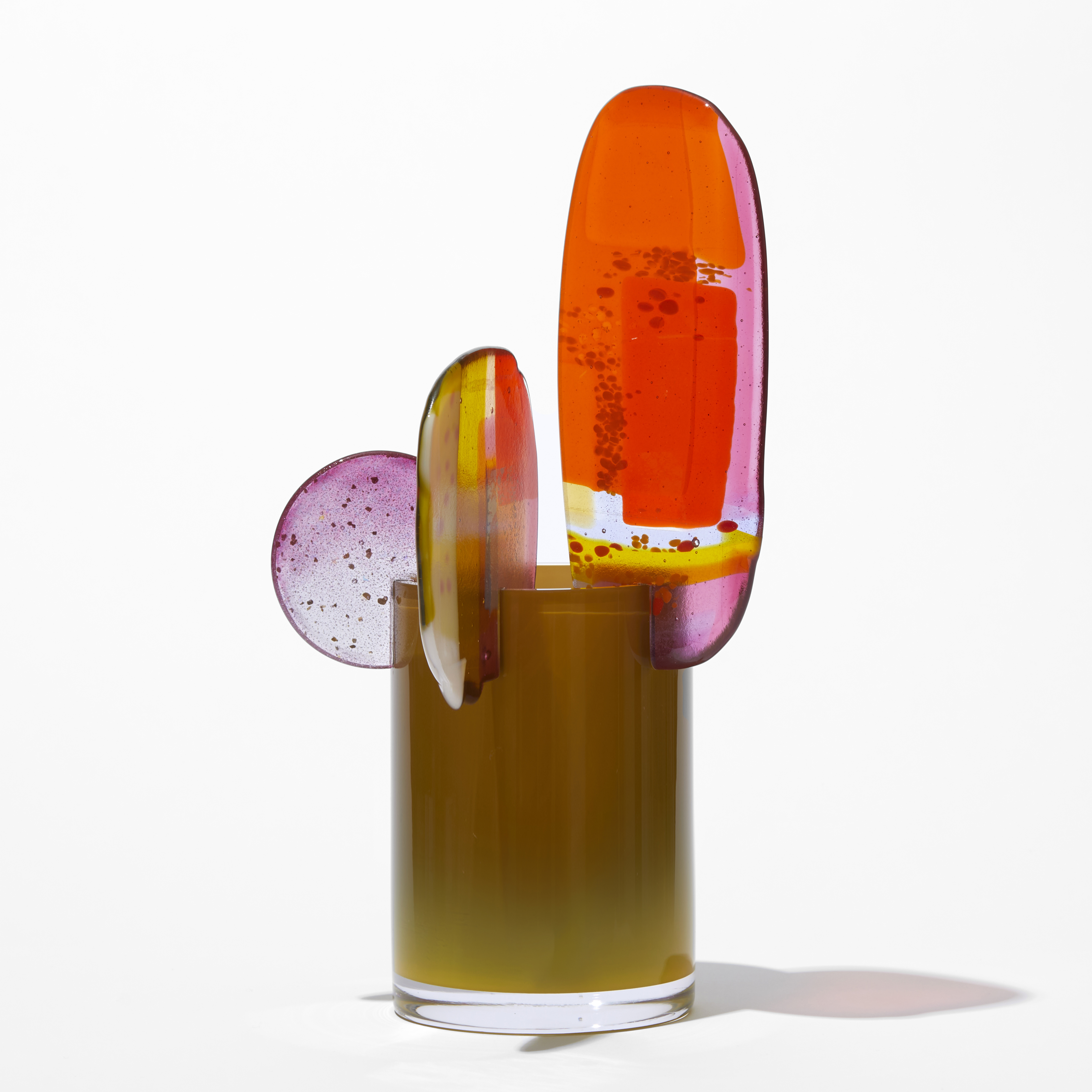 opaque khaki short tubular vase with three rounded finials in differing sizes overlapping and perched on the top rim in pink brown red gold yellow and clear hand made from blown and fused glass