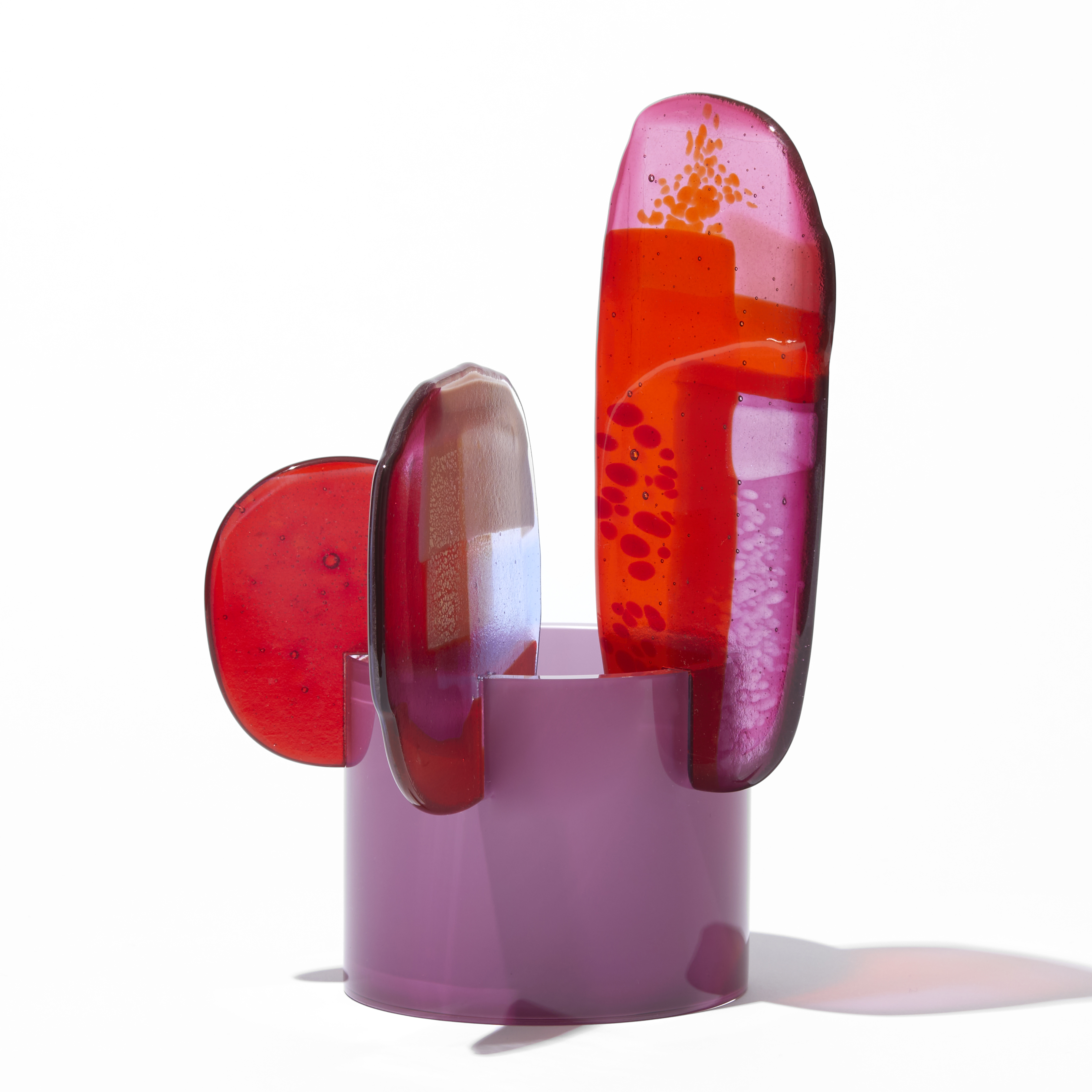 short opaque raspberry pink cylinder with three rounded different sized petals overlapping and perched on the top edge with abstract patterns in pink purple red and gold hand made from blown and fused glass