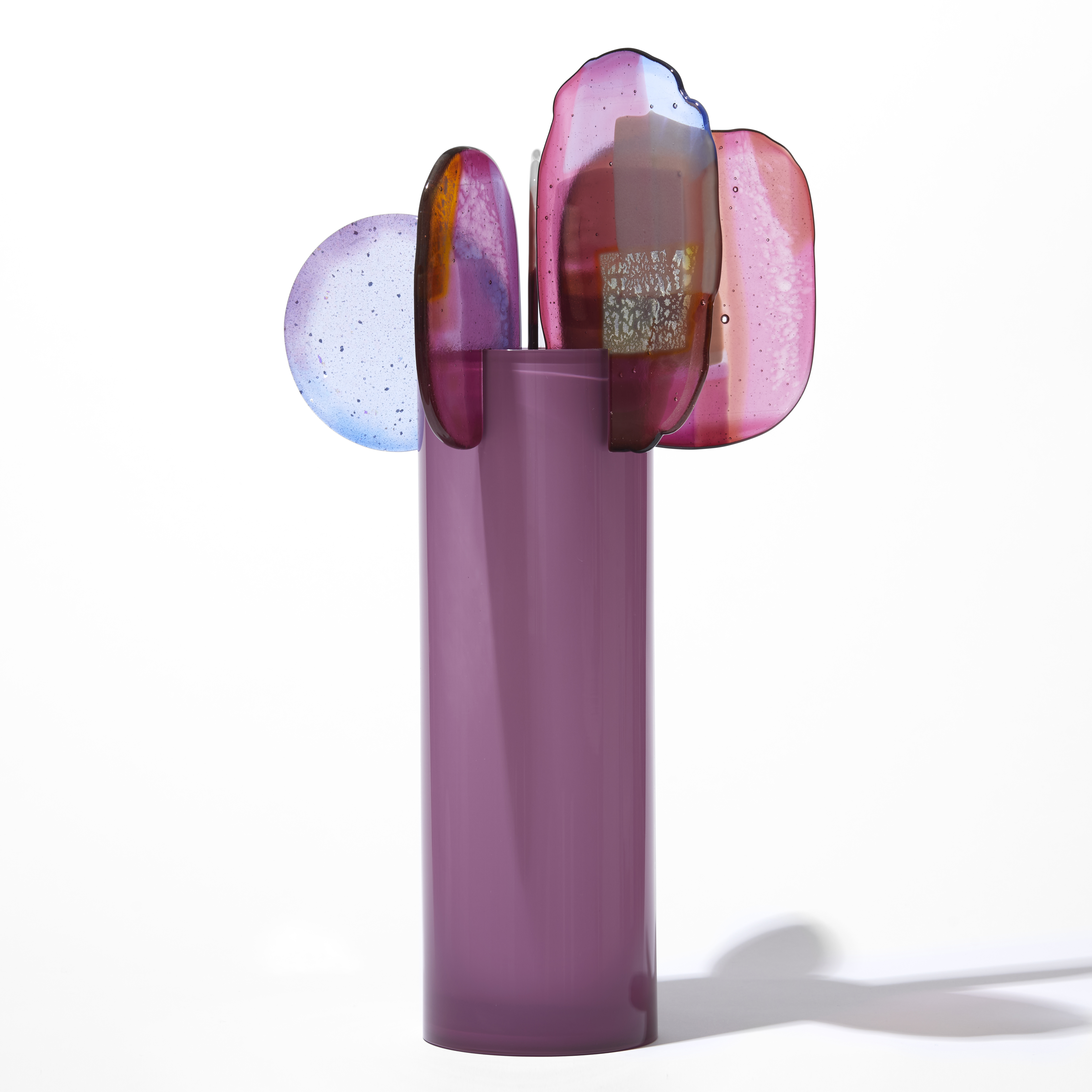 opaque raspberry pink cylinder with five rounded finals with abstract patterns in pink blue purple and gold perched on the top edge hand made from blown and fused glass