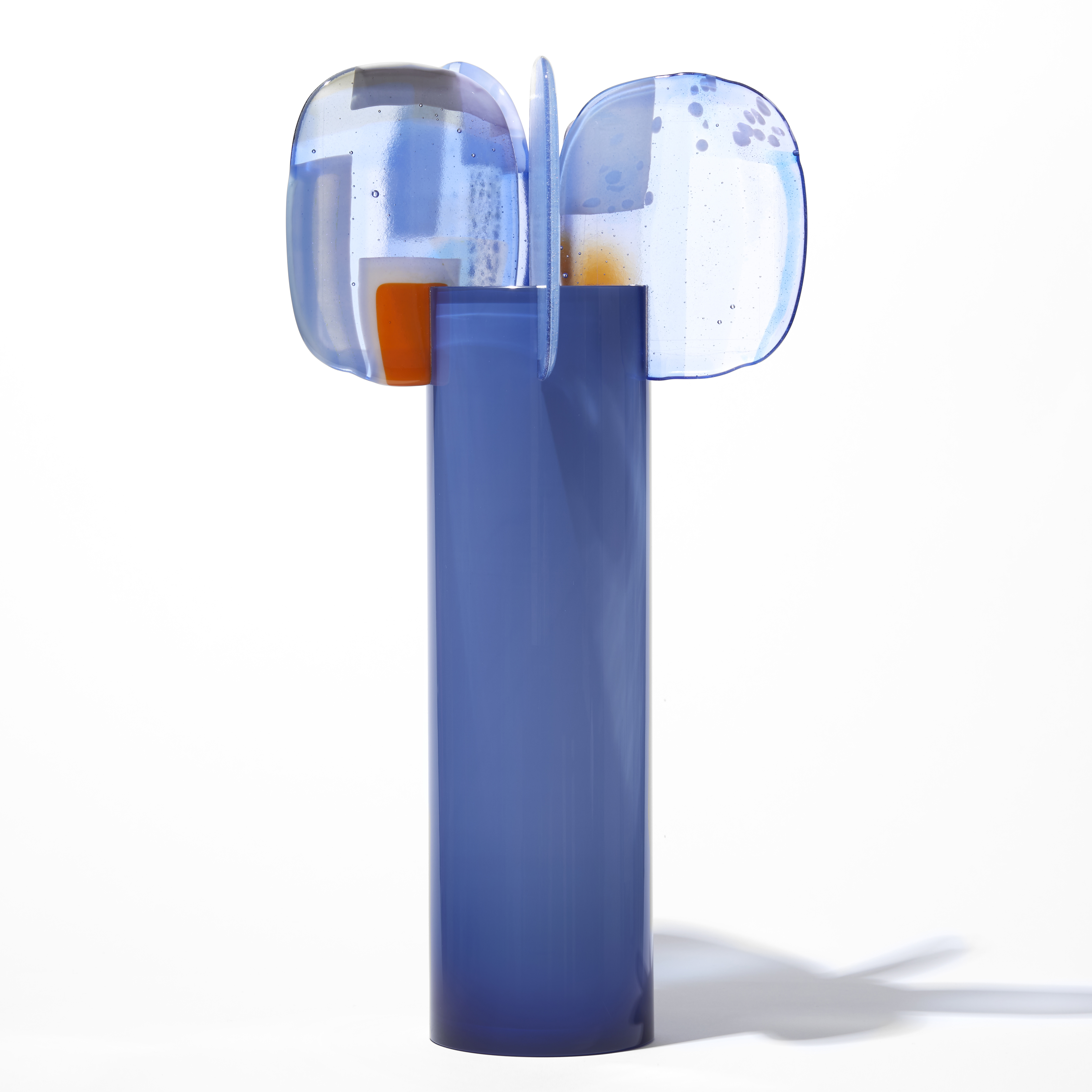 cornflower blue cylinder with five rounded abstract petal forms perched on top with patches of colour in red blue lilac and yellow hand made from blown and fused glass