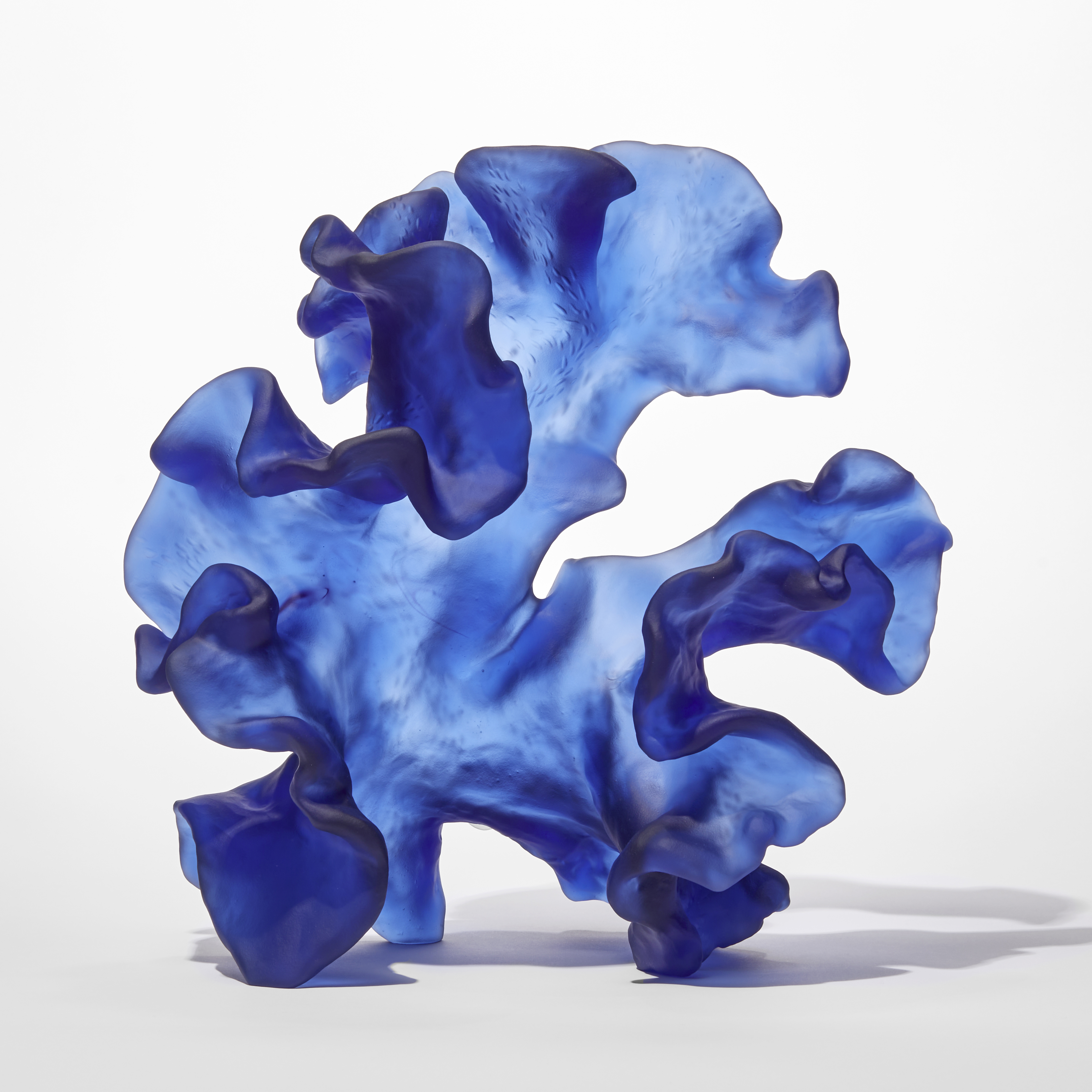 standing opaque blue frilled and undulating sculpture with the appearance of a piece of sea drift floating seaweed full of movement and made from cast glass