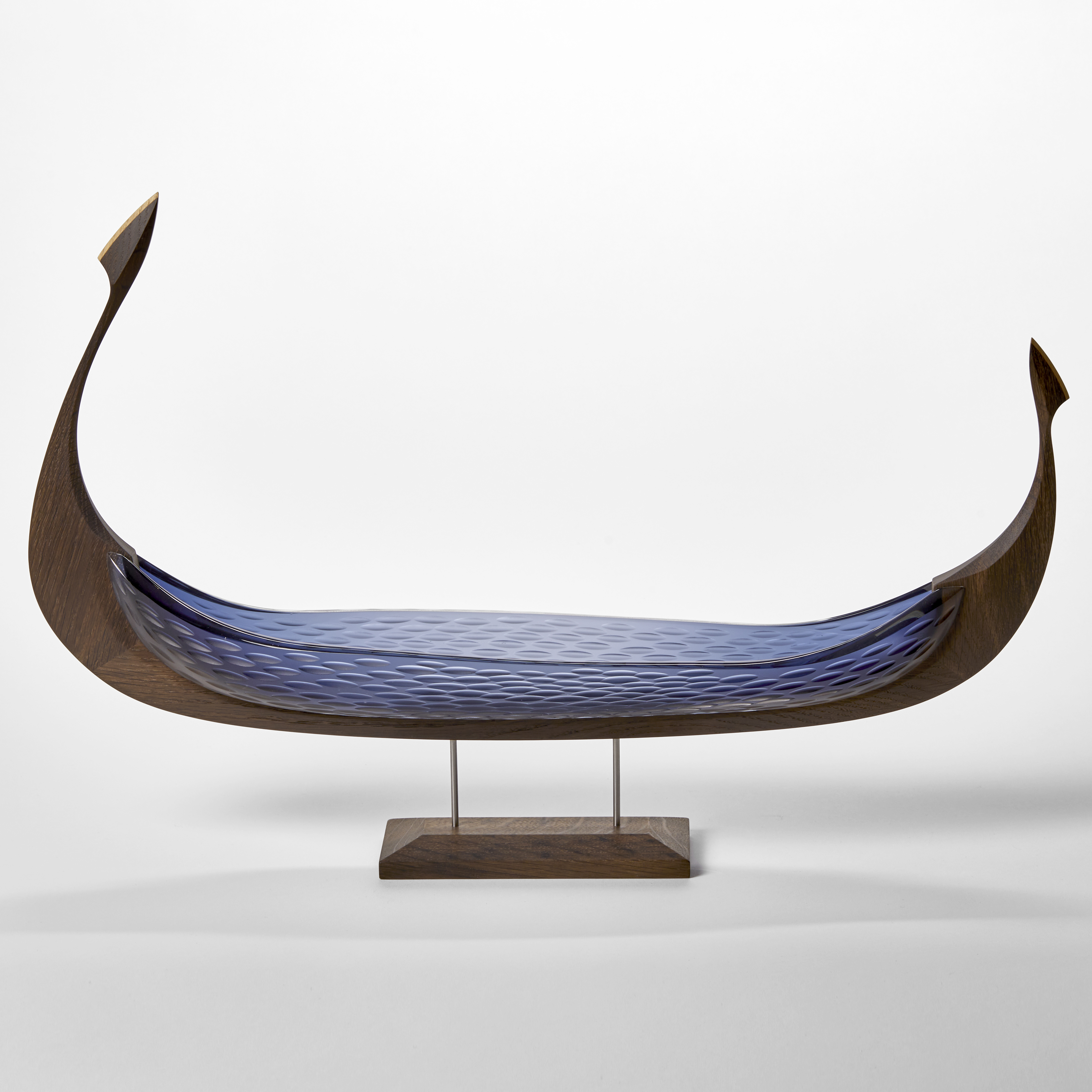 dark oak and opaque cut blue glass hulled viking ship with repeat cut texture pattern hand made and presented on a stainless steel and wooden base
