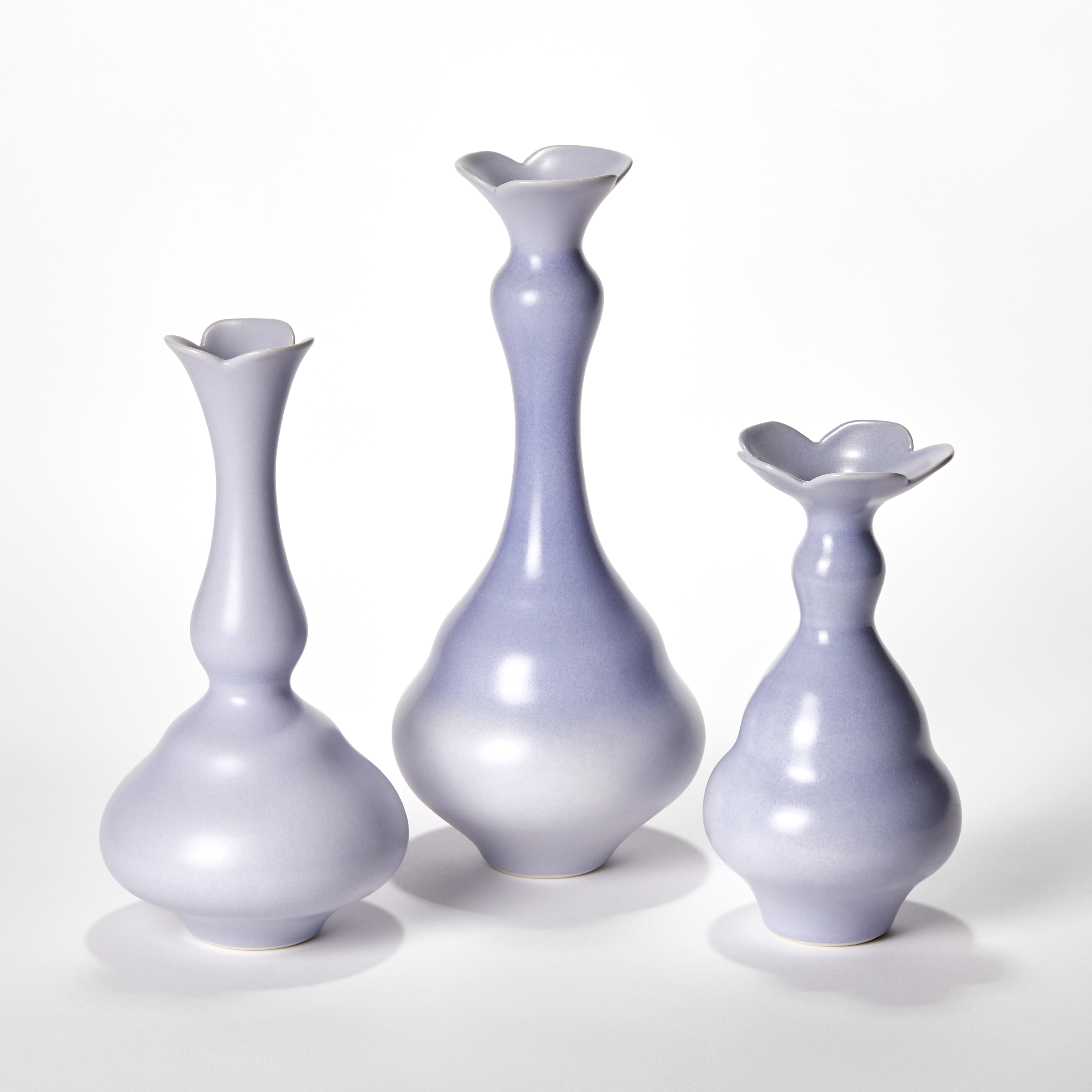 set of three porcelain vases in soft lilac purple each with wide rounded bases narrowing to long elegant necks each with abstract floral opening rims